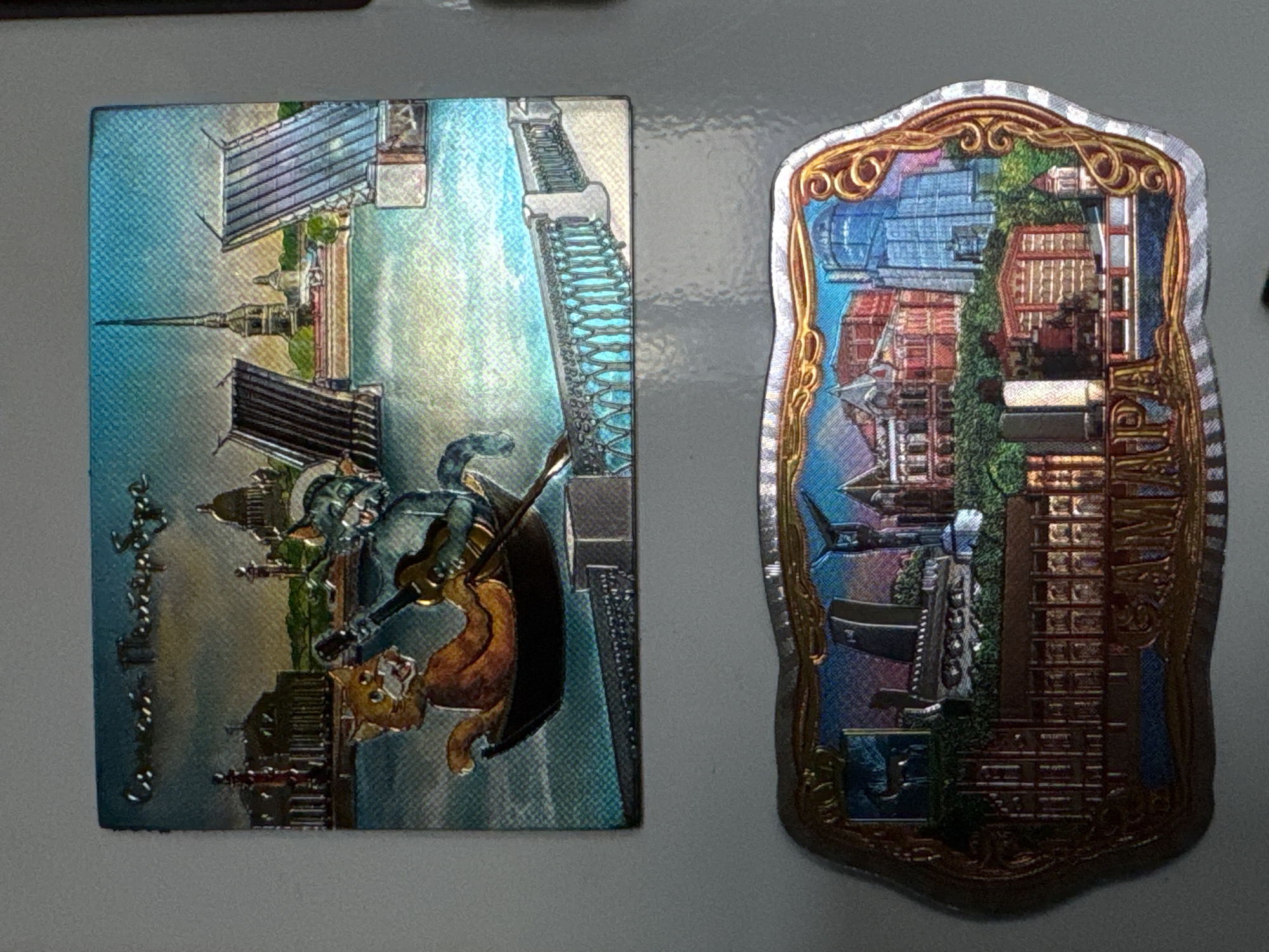 The image displays two refrigerator magnets. The top magnet depicts a scene in St. Petersburg, Russia, featuring a cat in a boat playing a guitar with another cat, set against a backdrop of iconic bridges and buildings like the Admiralty and St. Isaac's Cathedral. The bottom magnet showcases a cityscape with various architectural styles and a prominent inscription that appears to read "SAMARA," indicating it represents the city of Samara, Russia. There is no visual information connecting these magnets to the city of Izhevsk, Russia.
