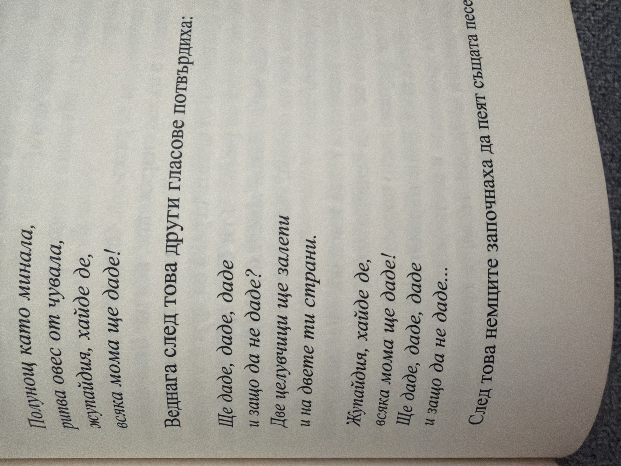 The image shows a page from a book with text in Bulgarian. The text appears to be a poem or song lyrics. The first stanza reads: "Полунощ като минала, / рипва овес от чувала, / жупайдия, хайде де, / всяка мома ще даде!" (Midnight when it has passed, / oats jump from the sack, / marry, come on, / every maiden will give!). The second stanza begins with "Веднага след това други гласове потвърдиха:" (Immediately after, other voices confirmed:). This is followed by lines about giving, kissing, and sides, and then the repetition of the phrase "Жупайдия, хайде де, / всяка мома ще даде! / Ще даде, даде, даде / и защо да не даде..." (Marry, come on, / every maiden will give! / Will give, give, give / and why not give...). The final visible line is "След това немците започнаха да пеят същата песен" (After that the Germans started singing the same song). The background is plain white, consistent with a book page. There is no visual information to determine a specific location in Pazardzhik, Bulgaria or any other city.