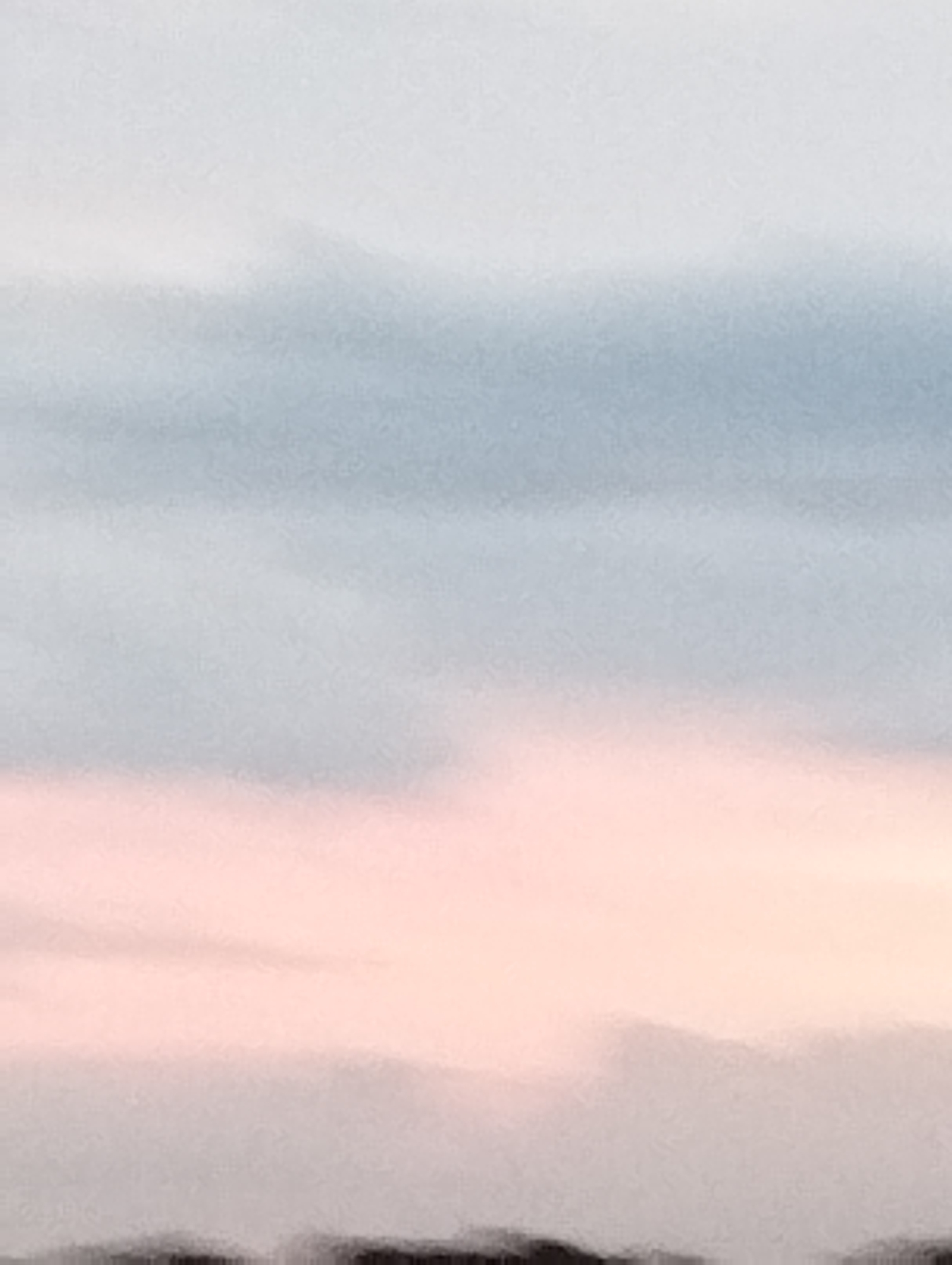 The image depicts a soft-focus, abstract scene with horizontal bands of color. The uppermost section is a pale, almost white blue, transitioning to a light gray-blue. Below this, a broad band of soft pink dominates the middle of the image, with subtle variations in hue. The bottom portion of the image is a darker, blurred band, suggesting a distant landscape or ground, rendered in dark gray and black. The overall impression is atmospheric and tranquil, possibly representing a sky at dawn or dusk. No specific landmarks or details of Ustyvytsia, Ukraine, are discernible. There are no people, subjects, objects, or actions depicted in the image.