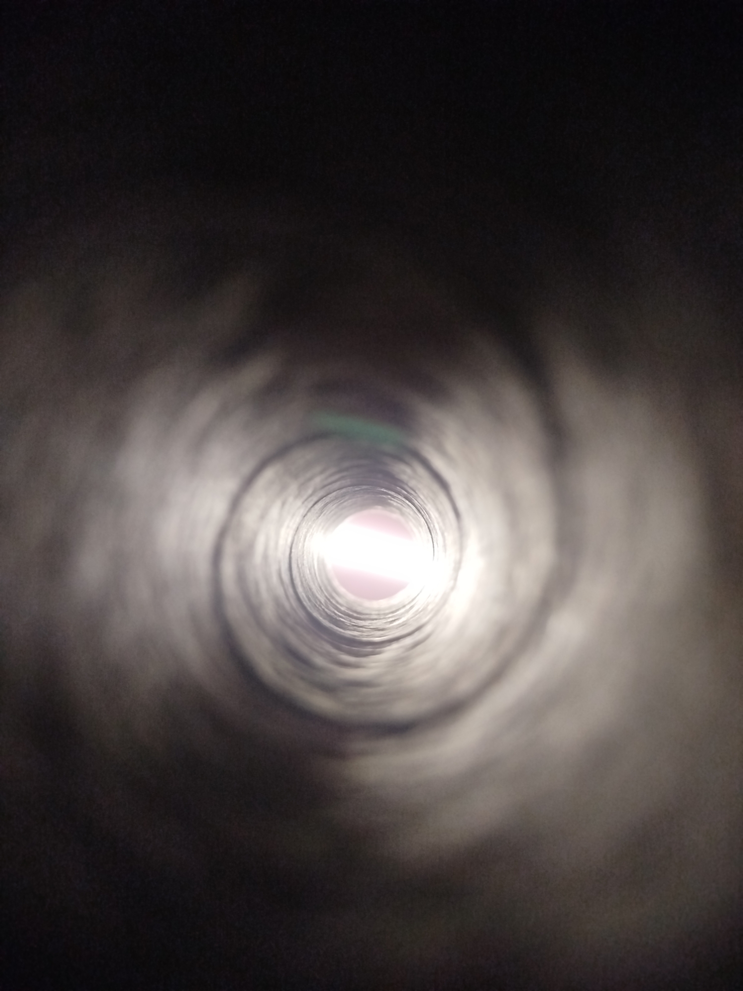The image depicts a dark, cylindrical tunnel with a bright light source at the far end, creating a tunnel vision effect. The interior walls of the tunnel appear to be textured and somewhat rough. The lighting suggests a transition from darkness to illumination. There is no visible indication of the city of Kremenchuk, Ukraine, or any people, subjects, objects, or actions. The scene is devoid of any contextual information that would place it in a specific urban environment.
