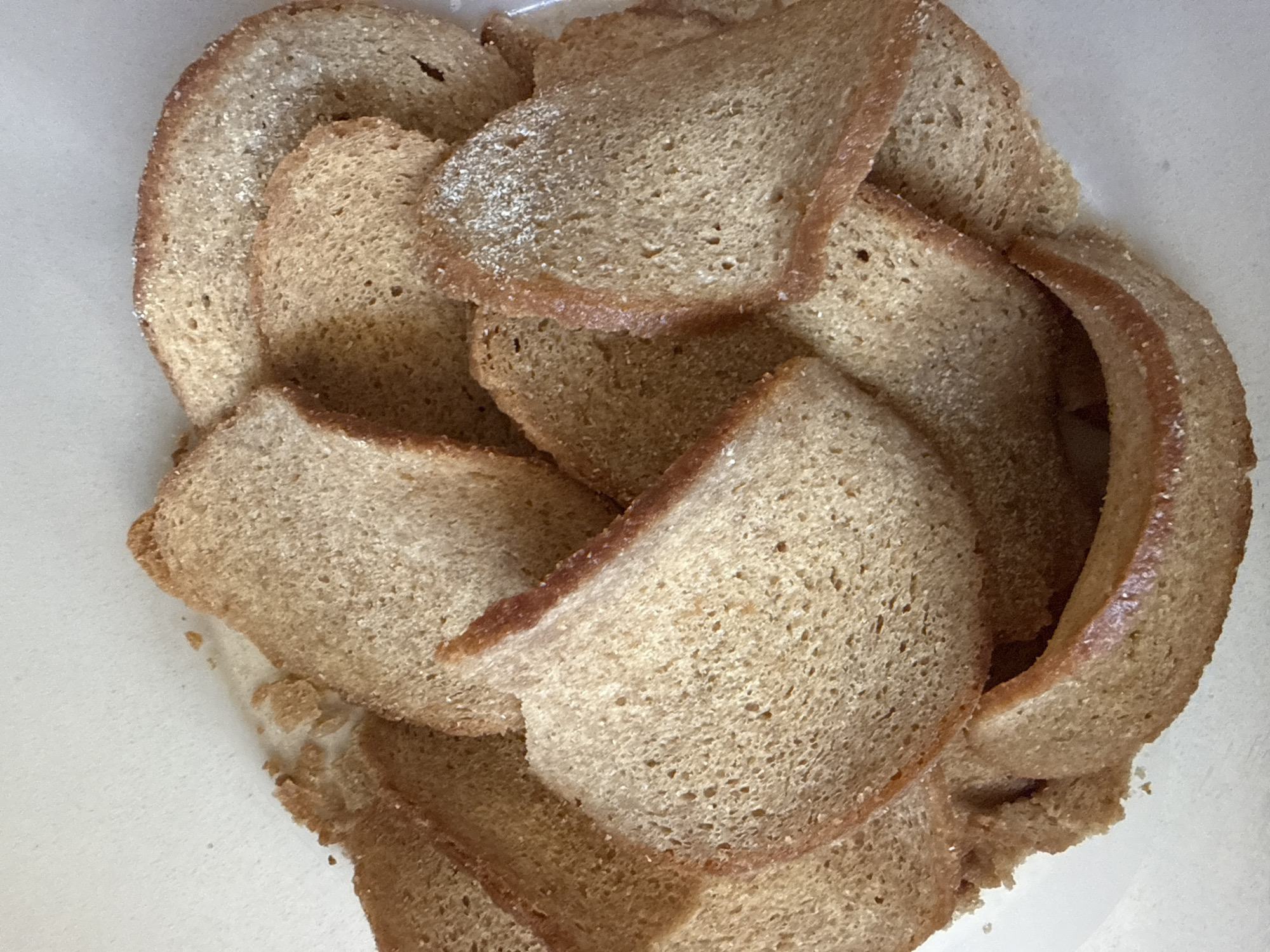 The image shows a pile of sliced brown bread. The slices are arranged in a haphazard manner, overlapping each other within a white container. The bread appears to be rye. There is no indication of a city or any further environmental context.