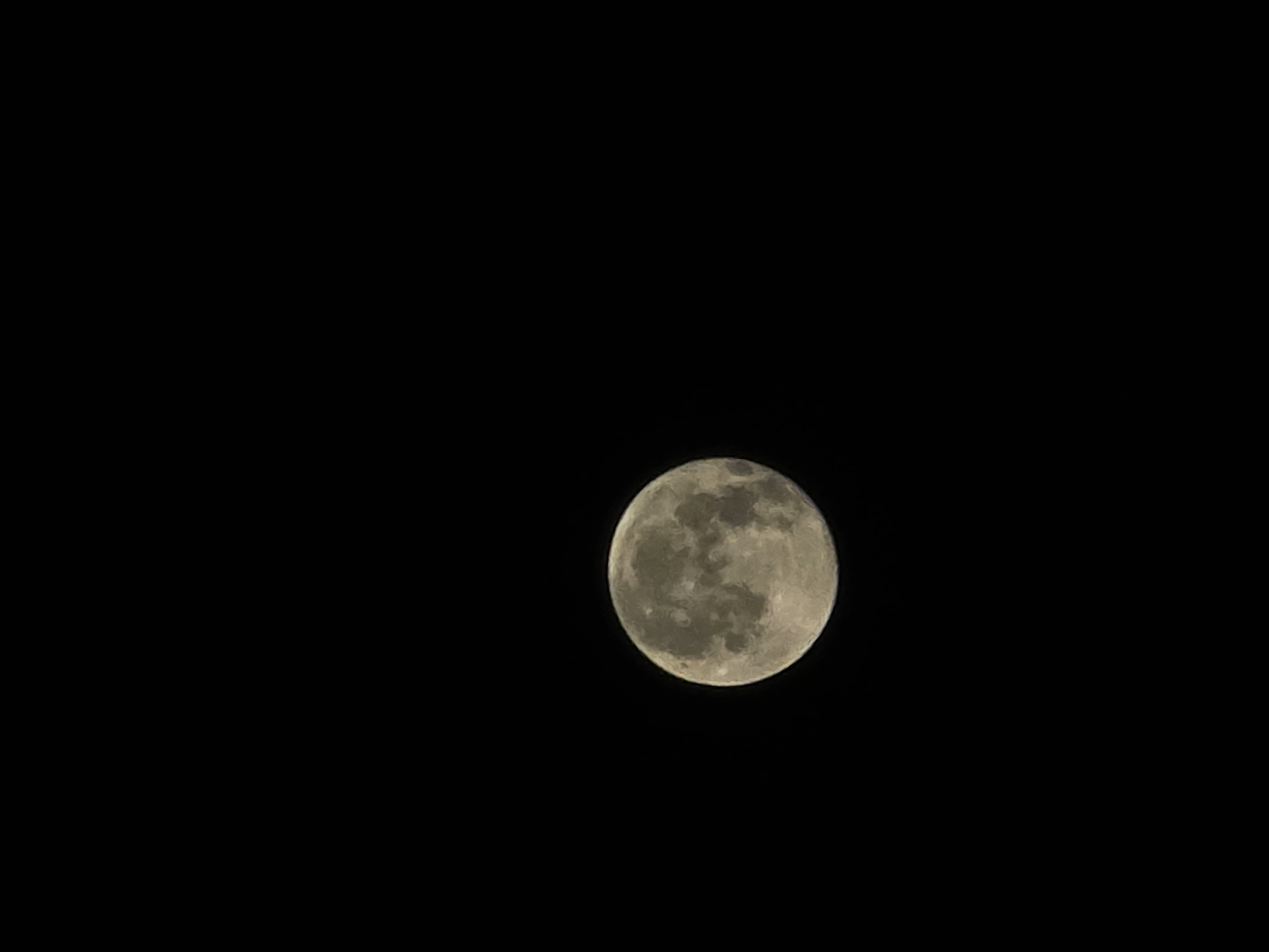 The image shows a full moon against a black sky. The moon is the sole object in the frame, positioned in the lower left quadrant. It is illuminated, revealing surface details such as craters and mare. The sky is completely dark, indicating nighttime. There is no indication of any urban environment, specific location in Yambol, Bulgaria, or any other contextual information.