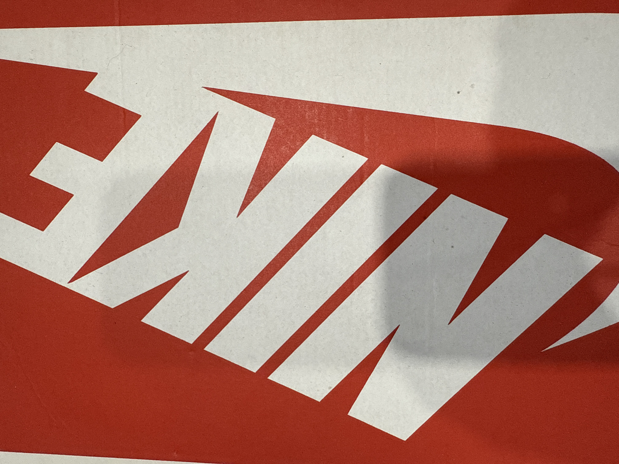 The image shows a close-up of the word "NIKE" in white letters against a red background. The surface appears to be textured, possibly cardboard. The lighting is somewhat uneven, with shadows visible on the right side of the image. The location in Votkinsk, Russia, is unknown, and there are no other details available.