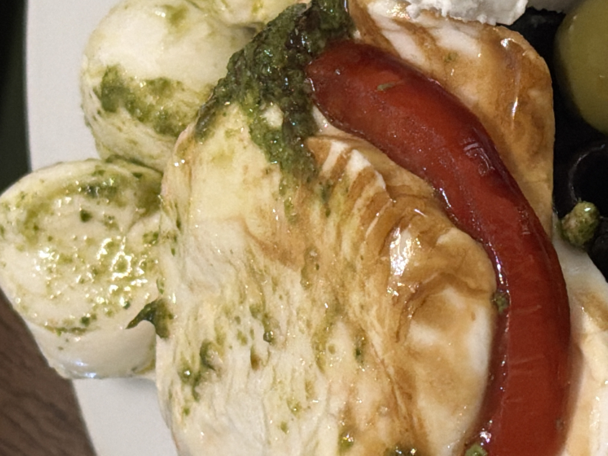 This is a close-up shot of a plate featuring Italian food, possibly caprese salad or a similar dish. On the left are small balls of mozzarella cheese covered in green pesto. To the right is a larger piece of cheese, also with pesto. A red pepper is draped over the cheese. The scene appears to be indoors, possibly in a restaurant. There is no indication of the location being Moscow, Russia.