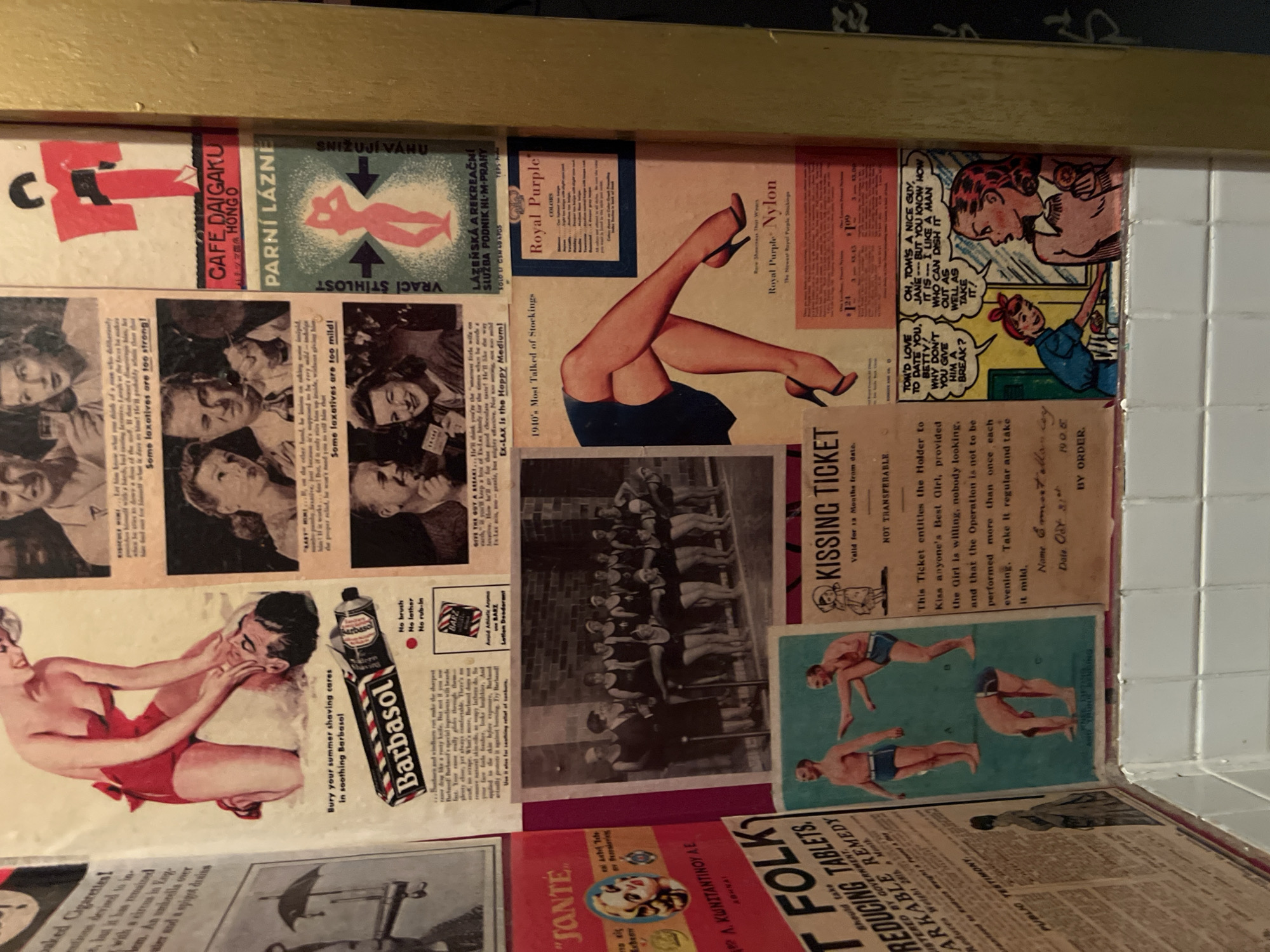 This image depicts a collage of vintage advertisements and comic strips arranged on a surface, possibly a wall or shelf within a room. The pieces feature a variety of subjects, including beauty and hygiene products, advertisements for nylon stockings and laxatives, and comic strip panels with romantic themes. There are also images of people, a group photo, and promotional material for a "Kissing Ticket." No information in the image indicates it is in Berlin, Germany.