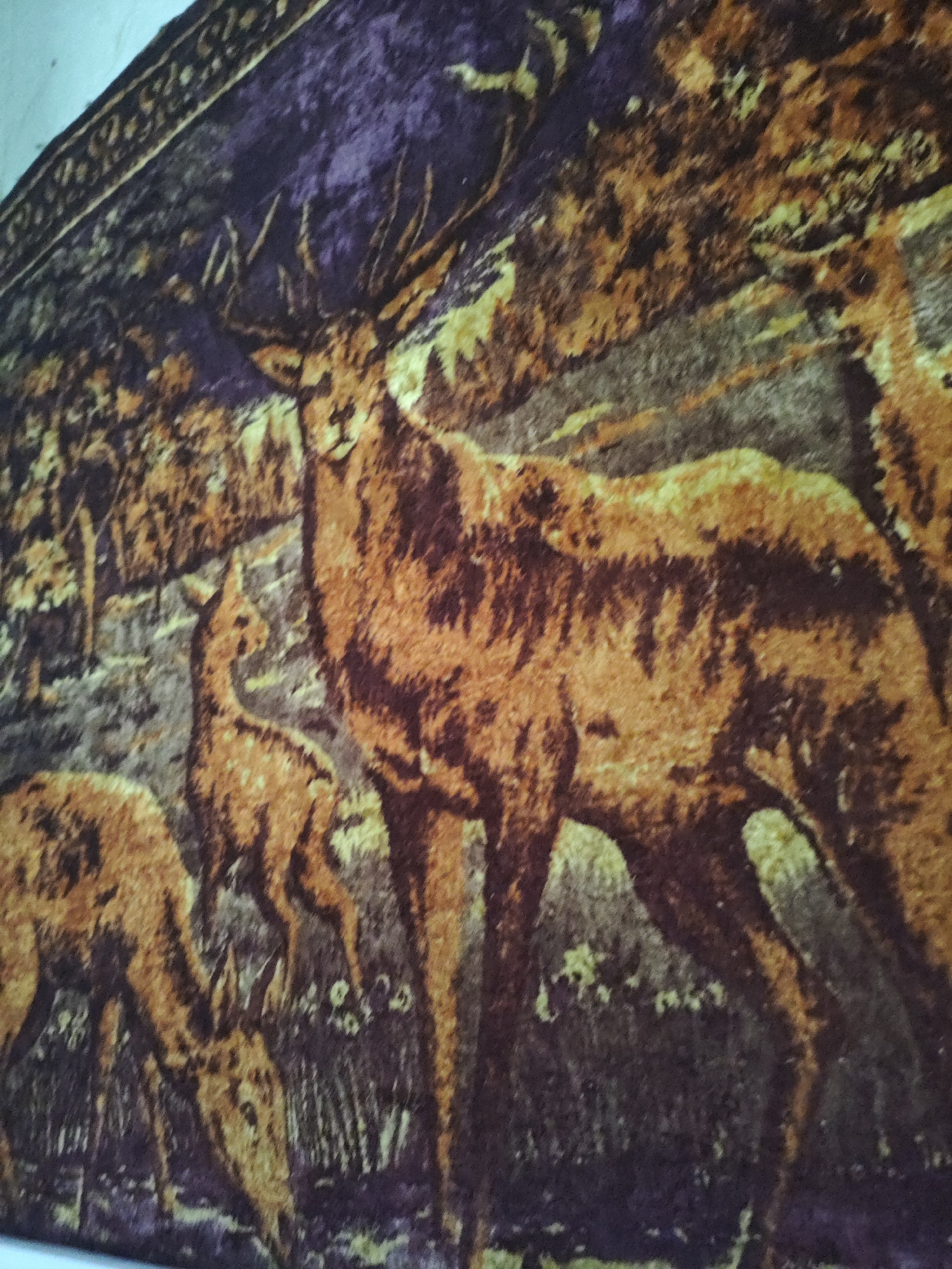 The image depicts a tapestry with a forest scene featuring deer. In the foreground, a large stag with impressive antlers is prominently displayed. To its left, two smaller deer are visible, one facing away and another partially obscured. The background suggests a wooded area with trees and undergrowth. The tapestry has a textured appearance, with the colors dominated by shades of brown, yellow, and purple. The exact location in Красназвёздаўскі сельскі Савет, Belarus, cannot be determined from the image alone as it is an interior shot of a decorative item.