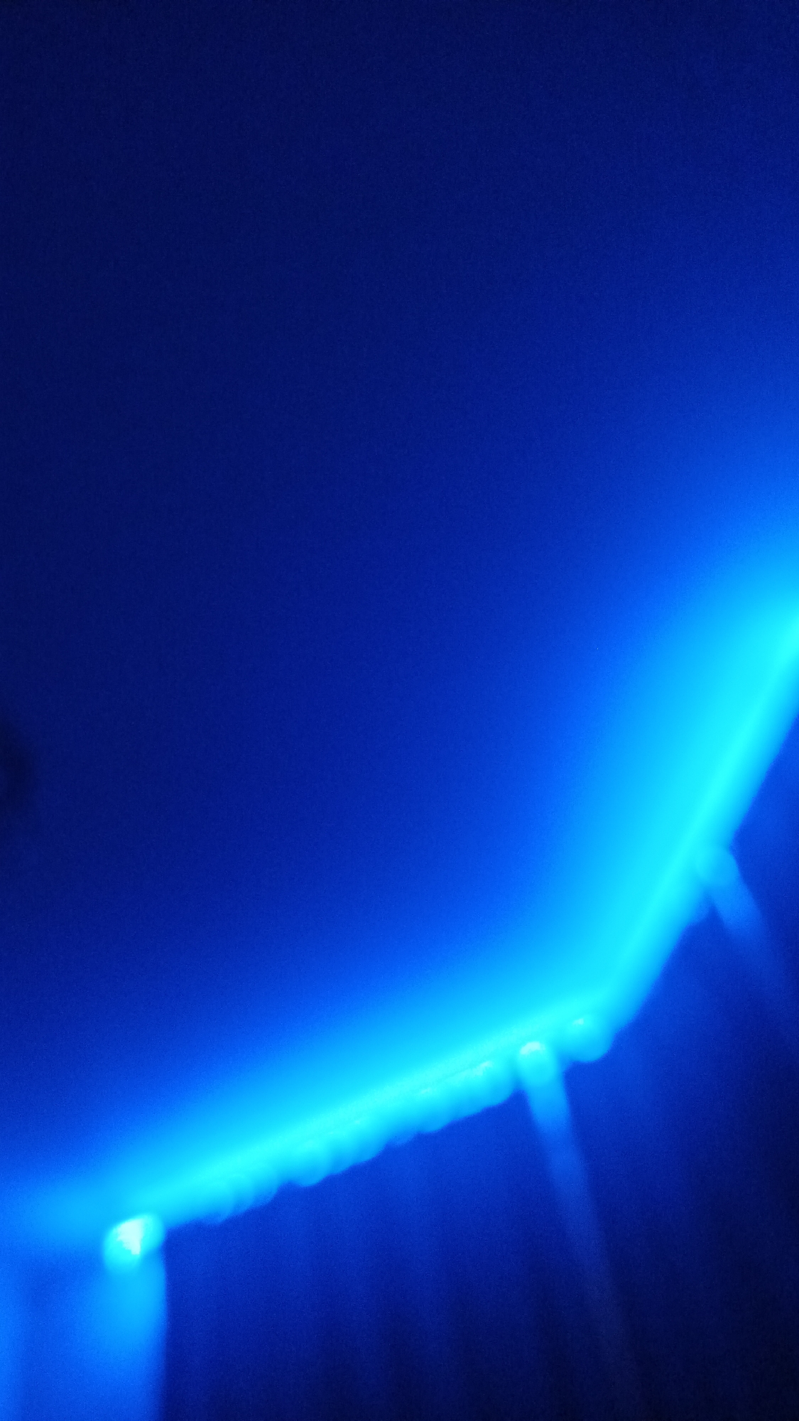 The image shows a dark blue, abstract scene illuminated by bright cyan LED lights. The lights appear to be positioned along an edge, casting beams downwards and creating a gradient of light that fades into darkness. There are no discernible objects, people, or actions visible. The setting is indeterminate and lacks any specific environmental features.