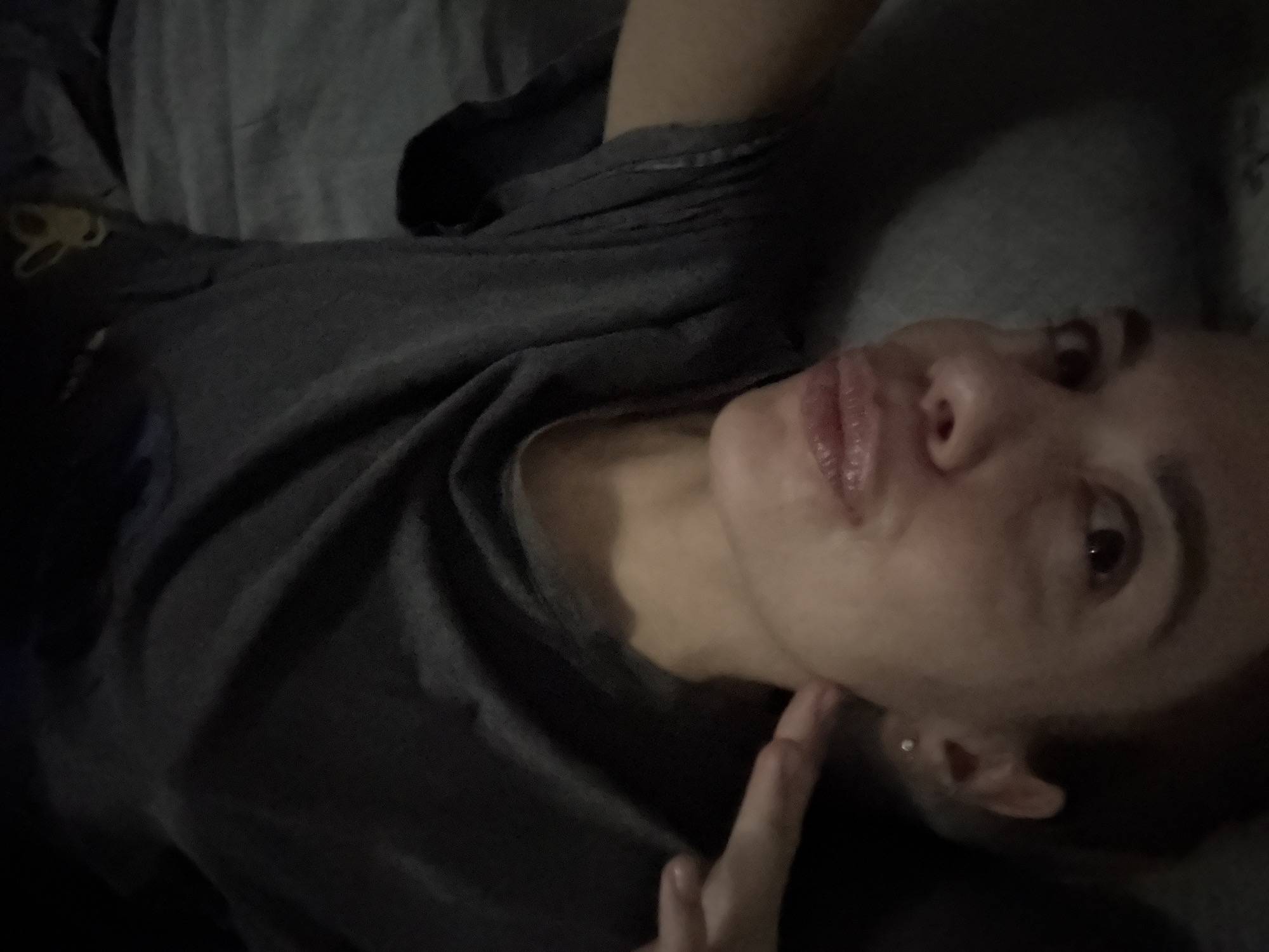 A person is lying down on a gray surface, likely a bed or sofa. The person is wearing a dark-colored t-shirt. One hand is visible, with a finger pointing towards the person's neck. The person is looking upwards. No location data is present in the image. Ust-Ilimsk, Russia is not related to the image.