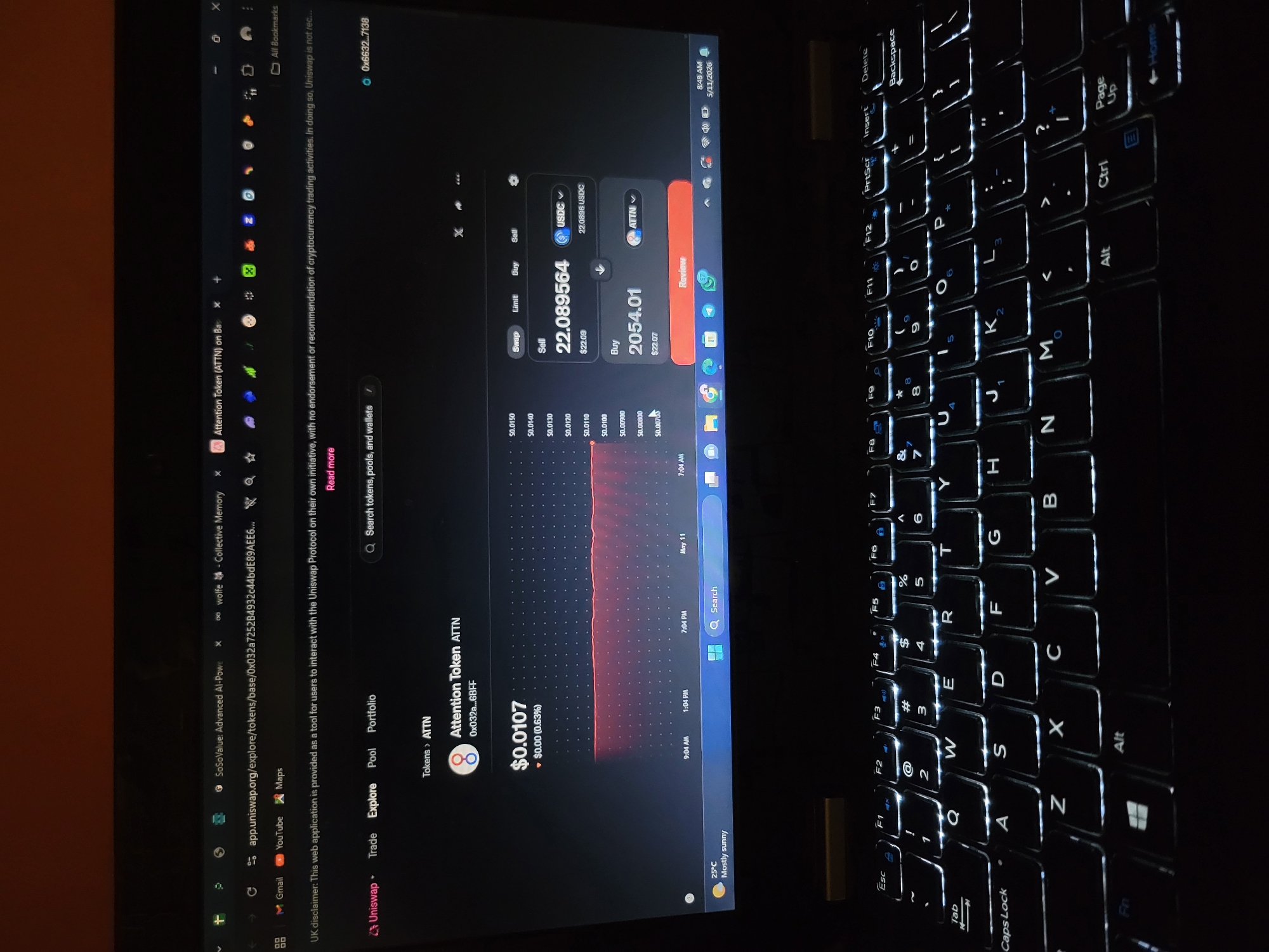 The image shows a dark room with a laptop open, displaying the Uniswap interface on its screen. The screen shows cryptocurrency trading information, specifically for Attention Token (ATTN), with its current price and trading details. The laptop's keyboard is illuminated with bright white backlighting, and the surrounding environment is dark. The date on the laptop's taskbar indicates it is May 11, 2026, at 8:48 AM. There is no indication of the city of Jos, Nigeria in the image. The focus of the image is the laptop screen and keyboard.