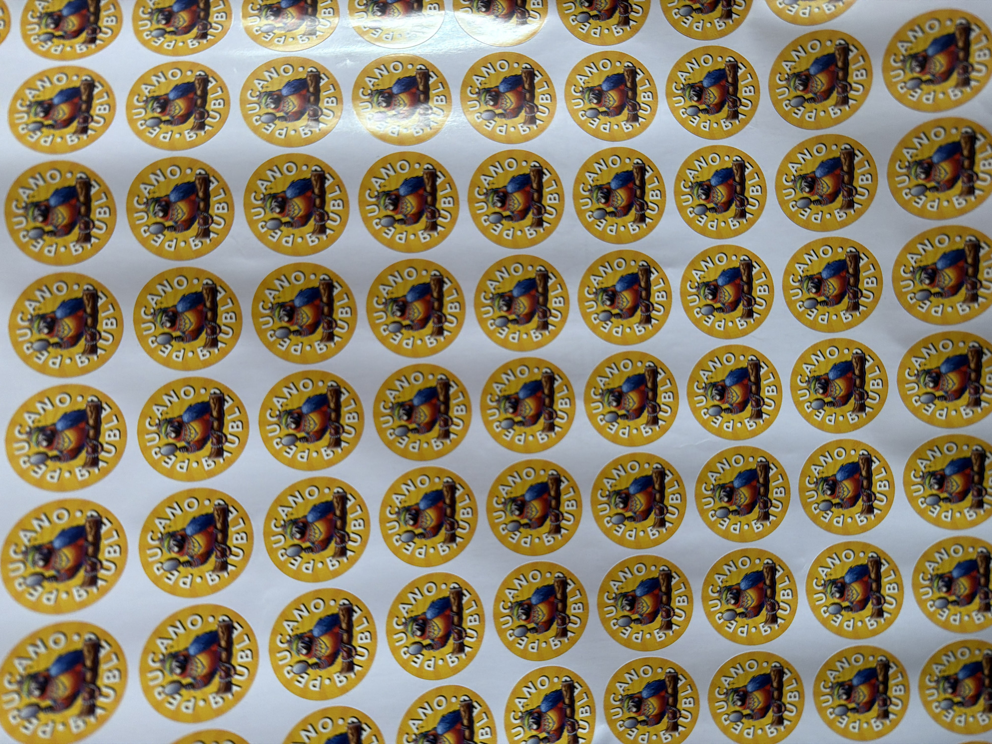 The image shows a sheet of circular stickers with a yellow background. Each sticker features a graphic with the words "BUCANO A.PE BUBLY" around the edge. The central image depicts a colorful cartoon-like figure or mascot of a parrot-like figure holding a spoon. The stickers are arranged in a grid pattern on the sheet. There is no indication in the image that the location is Khimki, Russia.