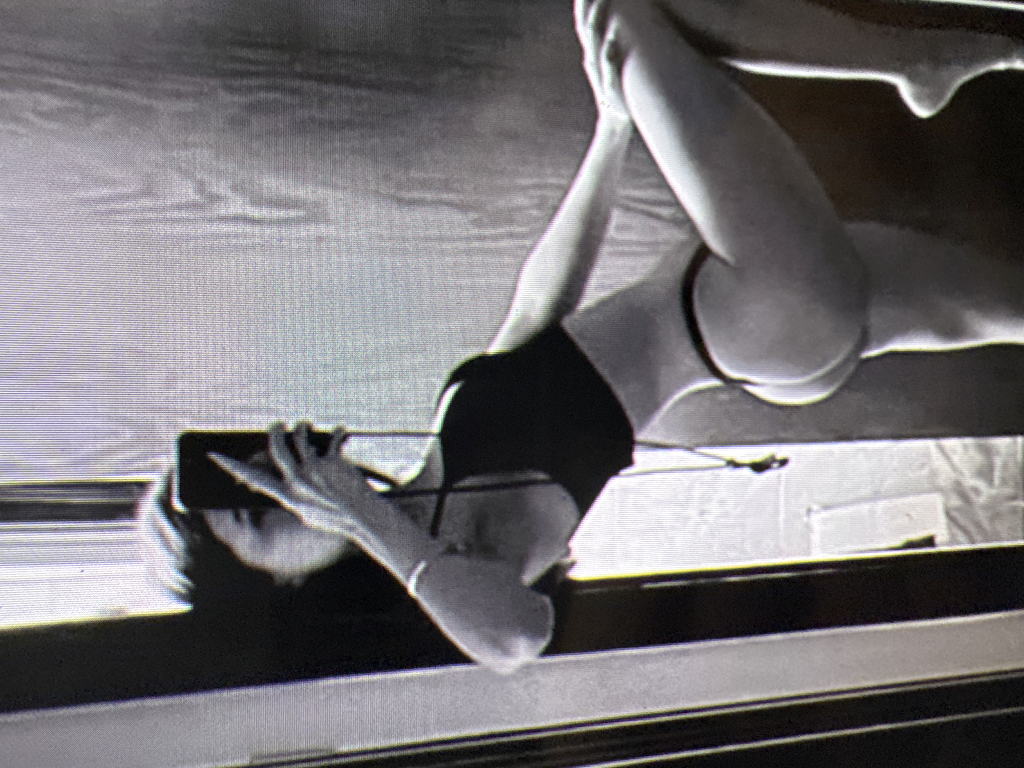 The image depicts a person taking a mirror selfie. The person is wearing a black bikini and is in a semi-reclined pose, with one leg extended. The background appears to be a room with a door and a textured wall, possibly a closet or wardrobe. The image quality is low, with a grainy texture and limited detail. There is no visible indication of the city of Castelo Branco, Portugal, or any other specific geographical location.