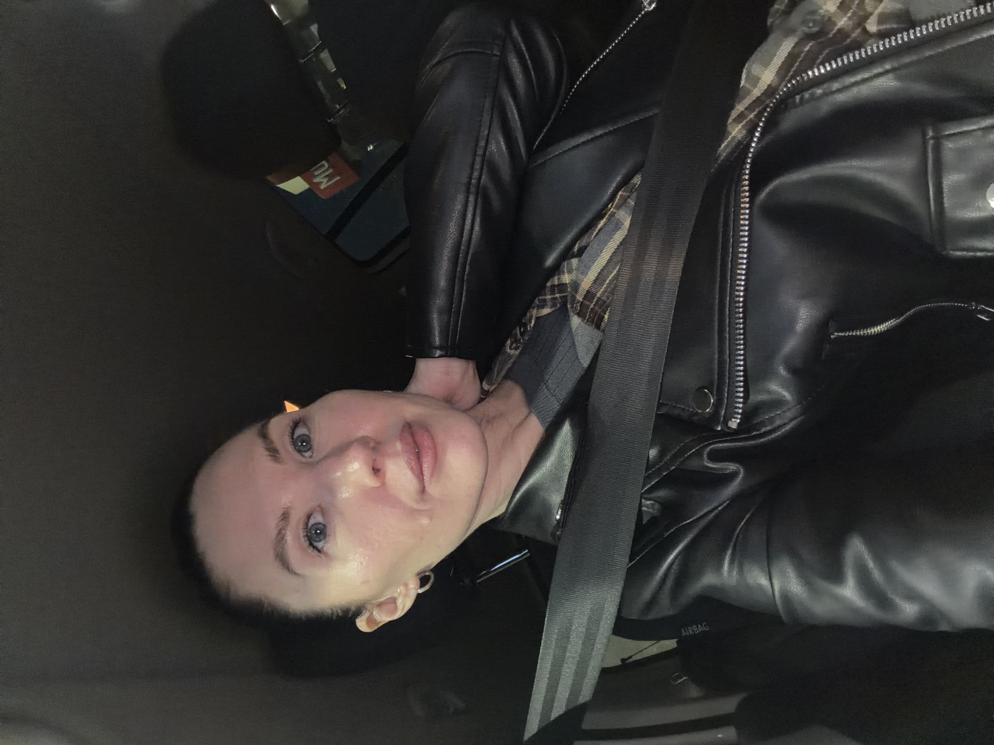 A person is in the driver's seat of a vehicle, wearing a black leather jacket and a gray and brown plaid shirt. They are wearing a seatbelt. The location is Perm, Russia, indicated by a sticker on the gear stick.