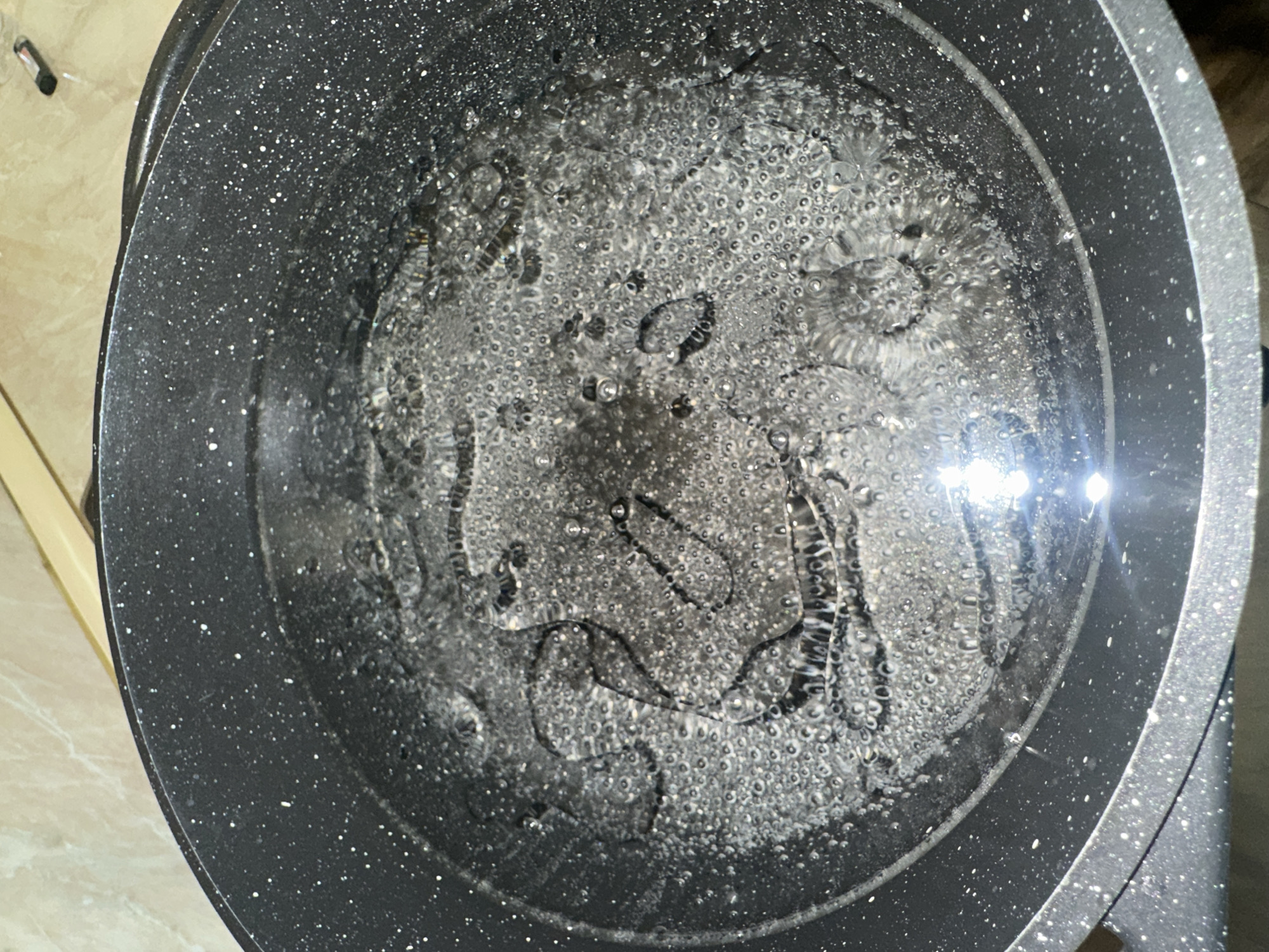 A top-down shot depicts water boiling in a speckled gray pot. No people are visible. The context suggests a kitchen environment. The location in Yerevan, Armenia, is not discernible from the visual information.