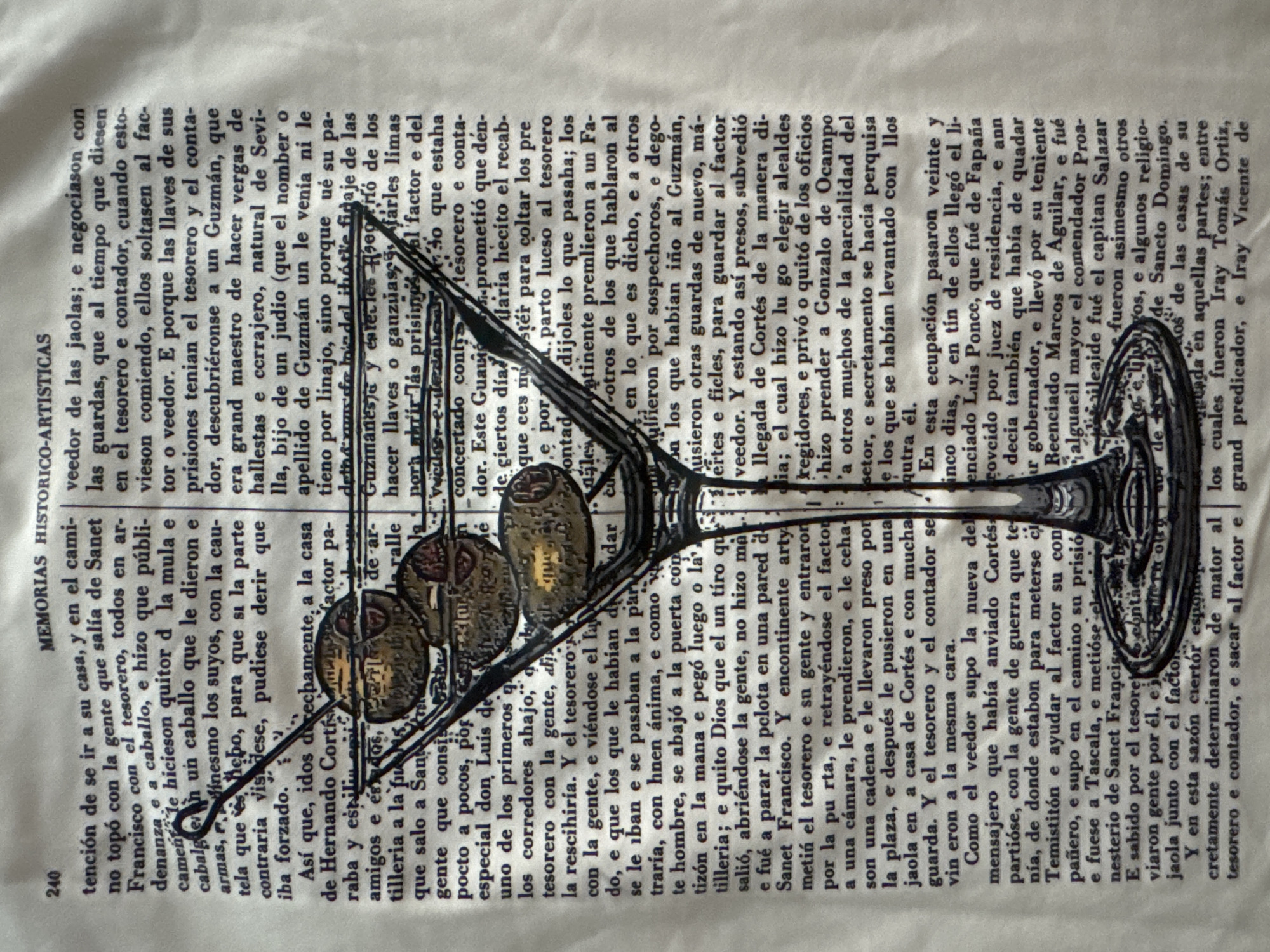 This image shows a close-up, high-angle shot of a martini glass with three olives, placed on top of a page of text. The text is printed in Spanish and appears to be from an old book or document. The page is textured and slightly discolored, suggesting age. The martini glass is clear and reflects the text underneath. The olives are green and appear to be intact. The background is out of focus, but it seems to be a continuation of the text page. There is no indication of the city of Sofia, Bulgaria in the image.