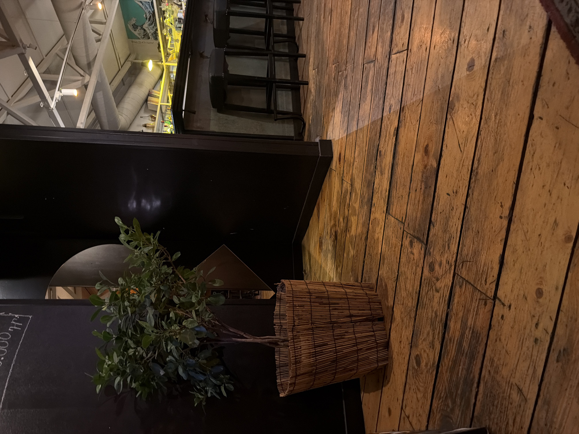 A potted plant stands on a dark surface near a wooden floor. The scene includes bar stools and glimpses of an industrial-style ceiling structure. It is difficult to verify the exact location in Yerevan, Armenia without additional context.