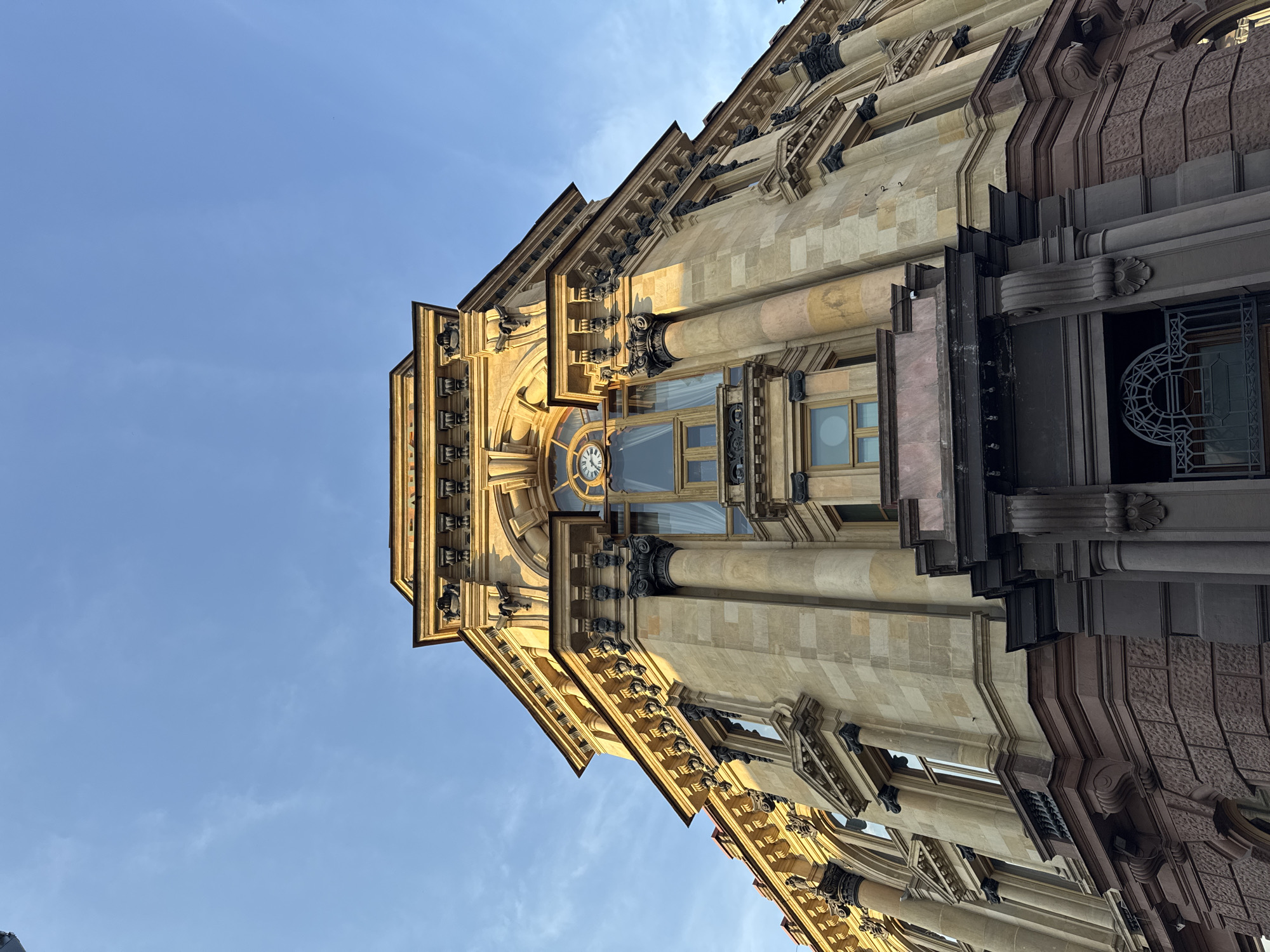 View of the Metropol Hotel in Moscow, Russia. The building is constructed of sandstone and features a clock tower. The sky is blue with faint clouds.