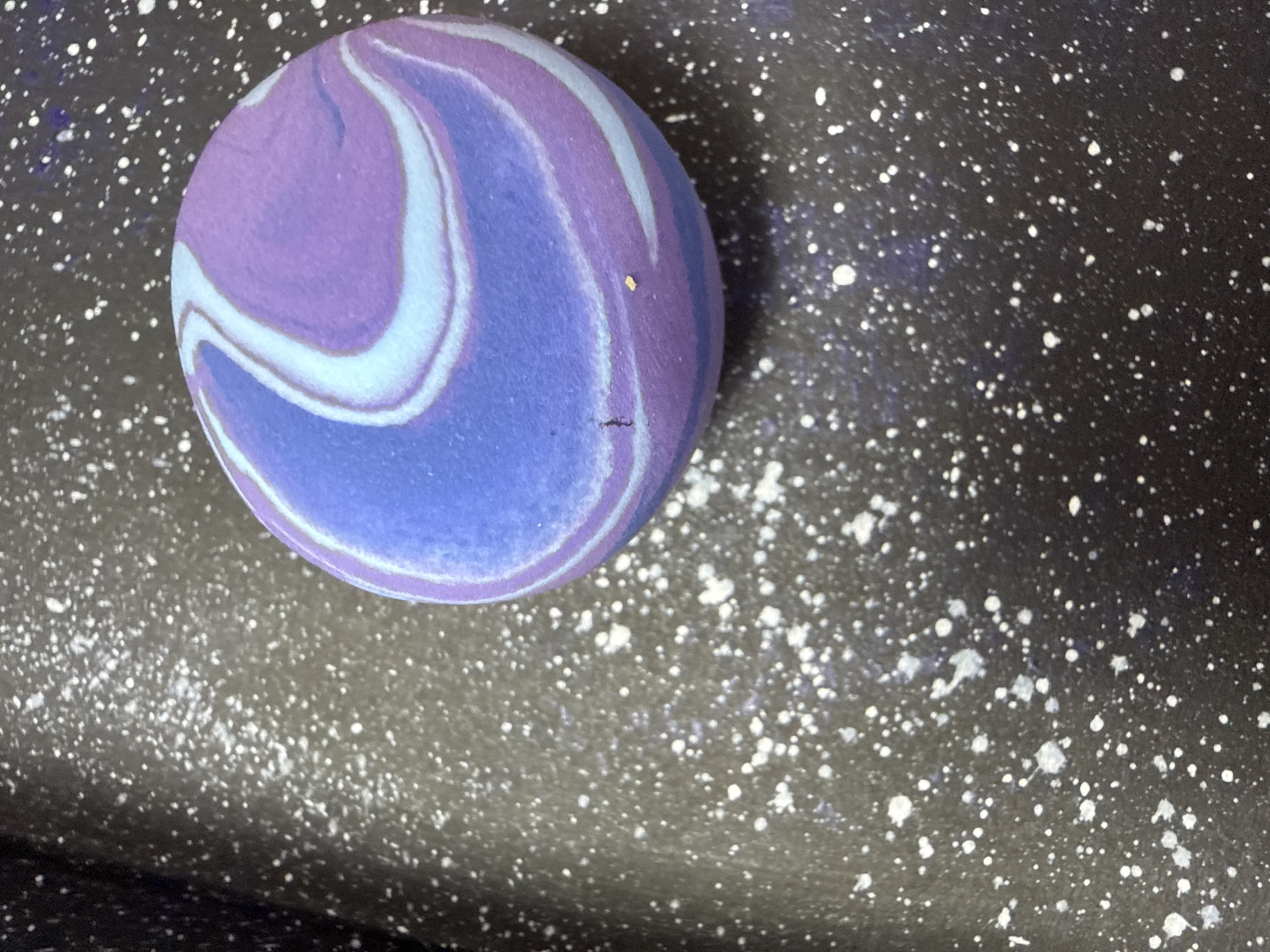 A round, purple and blue swirled object sits on a dark, speckled surface. The background surface appears to be a dark speckled black and white. The object appears to be sitting to the left of center. No people or landmarks are visible. There is no other identifiable information to link the location to Chaikovsky, Russia.