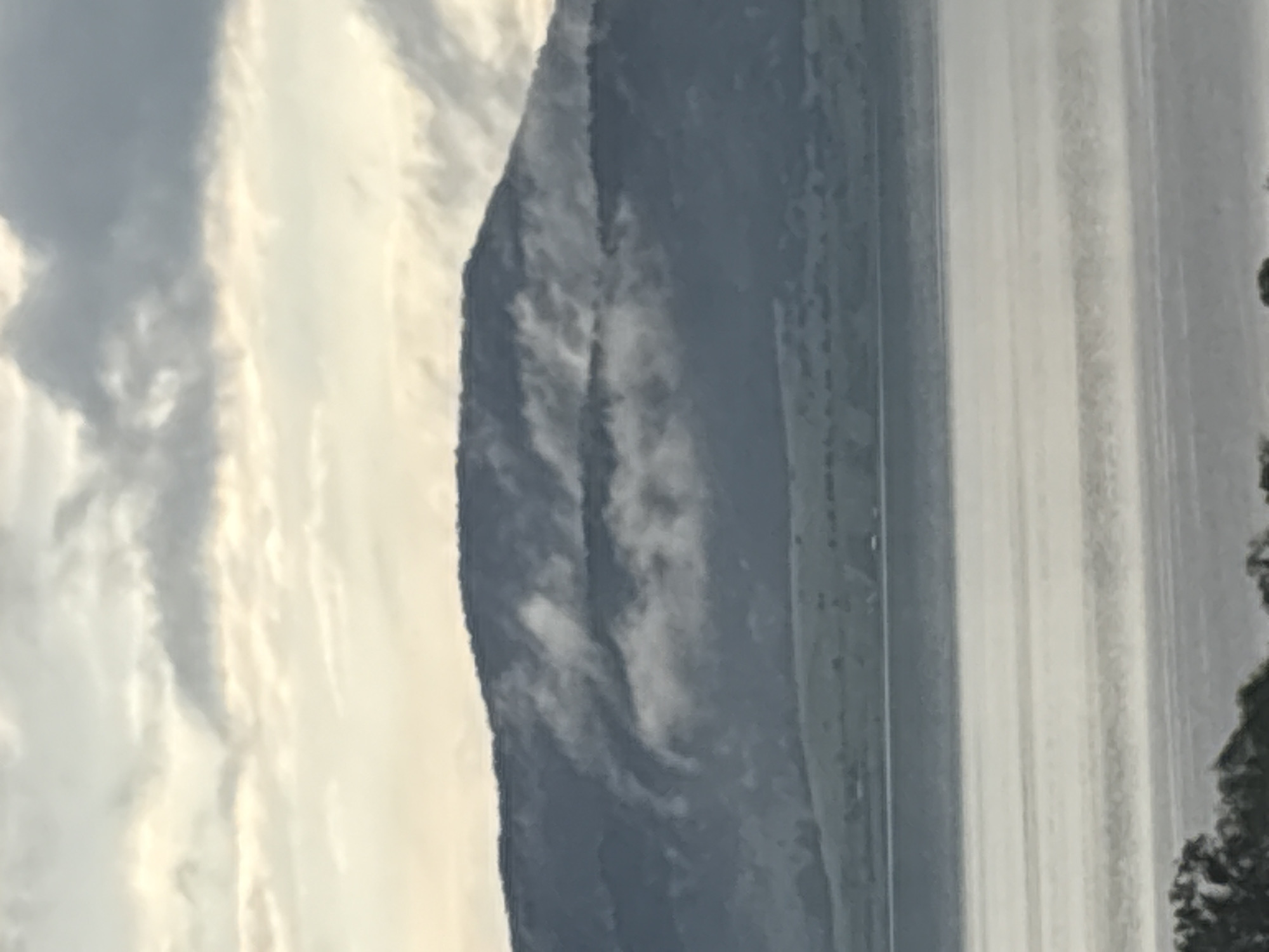 The image shows a view of a mountain range or large hill, possibly in the area of Tsigov chark, Bulgaria. To the left of the mountain, there are clouds. To the right, there appears to be a body of water or reflective surface, possibly a reservoir or lake. There are also some trees or foliage visible on the far right.