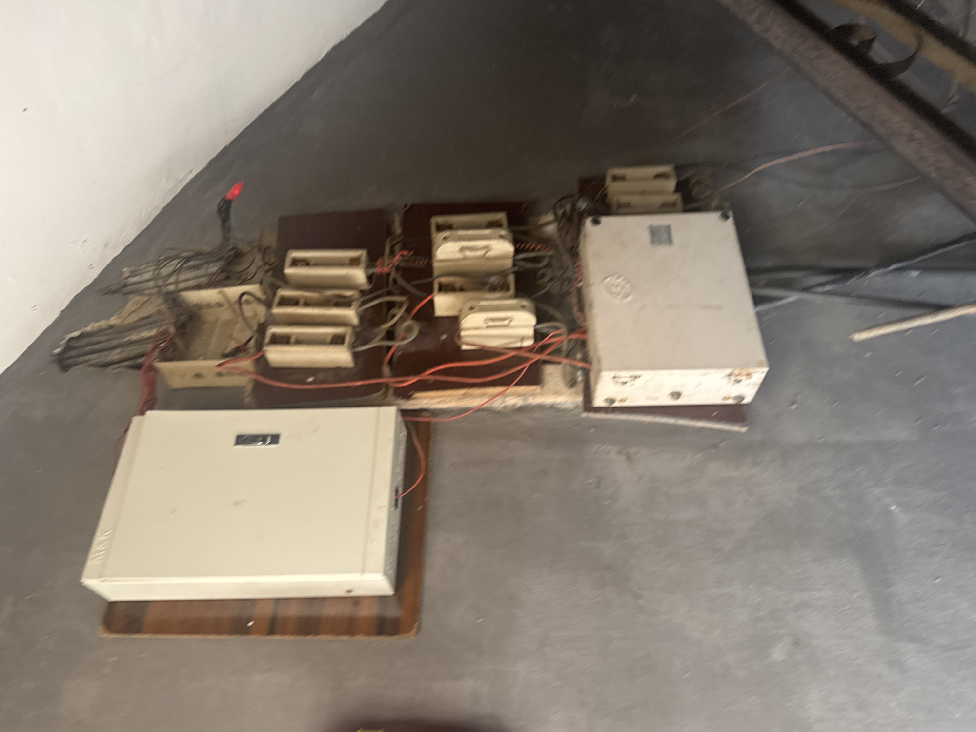 The image shows a cluster of telecommunications equipment on a concrete floor in Ihiagwa, Nigeria. There are several white and beige boxes with exposed wiring and connections. The equipment appears to be outdated and disorganized. The setting is a poorly lit, possibly industrial or storage area. No people are visible.