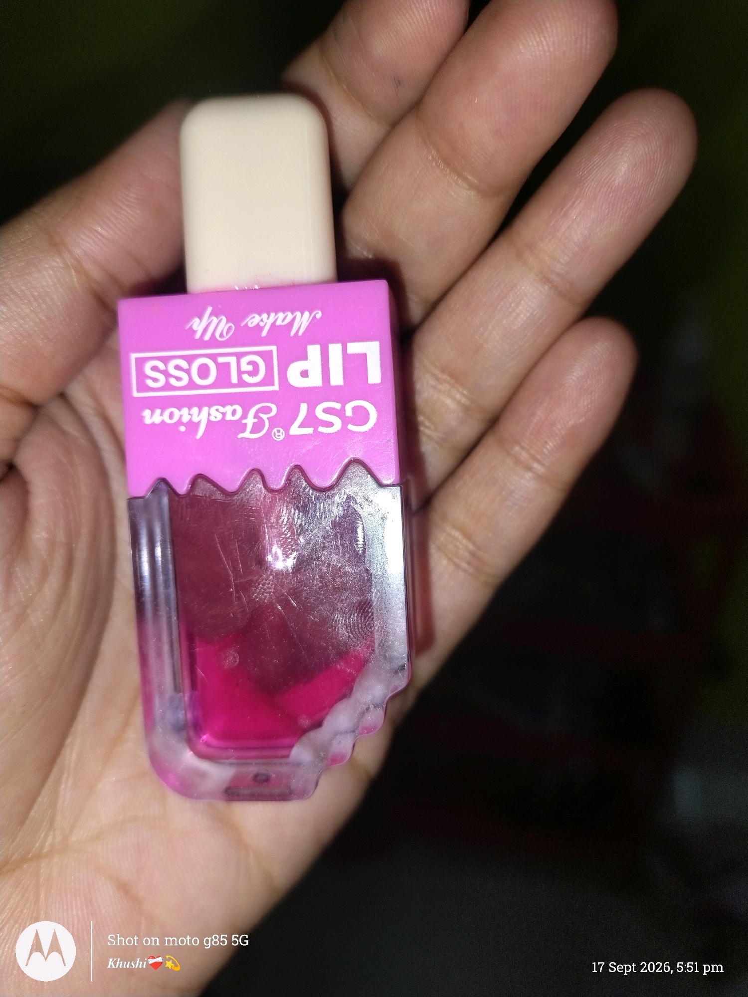 A person is holding a small, pink, rectangular bottle of "GS7 Fashion LIP GLOSS Make Up" in their palm. The bottle contains a bright pink liquid. The bottle has a white cap. The background is dark and out of focus. A timestamp in the lower right corner reads "17 Sept 2026, 5:51 pm". There is no identifiable information about the location in Barrackpore, India.