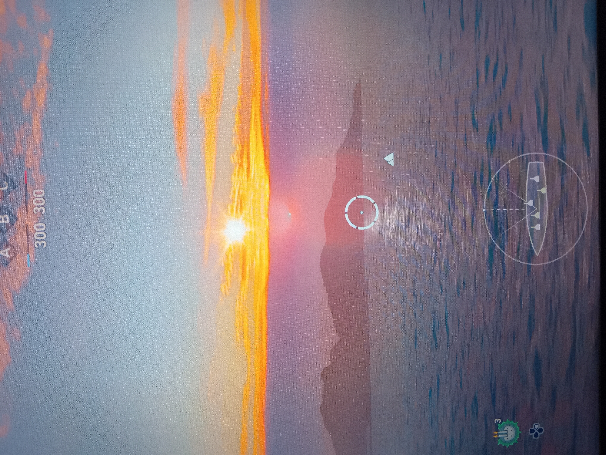 This media file is a photograph of a video game screen, depicting a serene yet active scene during either sunrise or sunset over a body of water. The dominant feature is a brilliant, glowing sun low on the horizon, casting a strong light that creates fiery orange and red hues across the sky and reflects intensely on the water's surface.
The sky transitions from vivid orange and red near the sun to a softer blue and grey further away, with some cloud formations visible. A distant landmass, possibly a mountain or island, is silhouetted against the bright light of the horizon, appearing dark and jagged. The water, likely an ocean or large lake, reflects the vibrant sky, creating streaking patterns of light and color.
Numerous user interface (UI) elements are visible, suggesting gameplay. In the upper left corner, the letters "A B C" are displayed, with 'A' highlighted in red, accompanied by the numbers "300 - 300". Towards the center of the screen, a white circular reticle or crosshair is present. To its right, a small white triangular indicator points towards the sun. In the lower right, a circular mini-map or compass shows the outline of a ship, facing forward, with multiple smaller indicators, possibly representing other vessels or objectives. At the bottom center, two distinct icons are visible: one green, shield-shaped with a skull-like emblem and the number '3' beside it, and another smaller, grey icon resembling an explosive device. The overall image displays a pixelated grid pattern typical of a screen photograph.