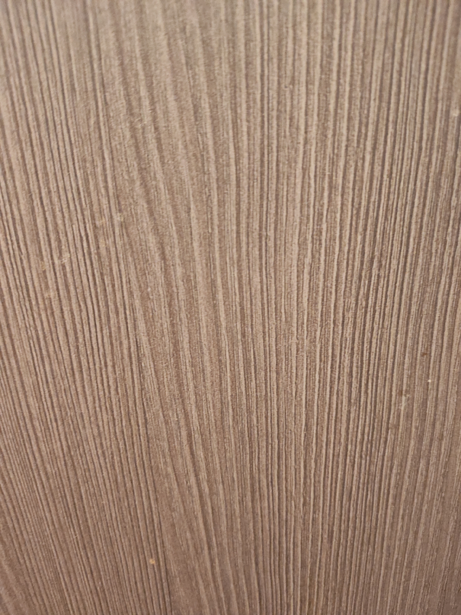 The image shows a close-up, abstract view of a textured surface. The texture consists of numerous fine, parallel vertical lines that appear to be either carved or naturally occurring in the material. The color of the surface is a muted, light brown or beige. There are no discernible objects, people, or environmental elements visible that would indicate a specific location within the city of Малое Верево, Russia, or any other location. The image is a detail shot focusing solely on the textural pattern of an unknown material.