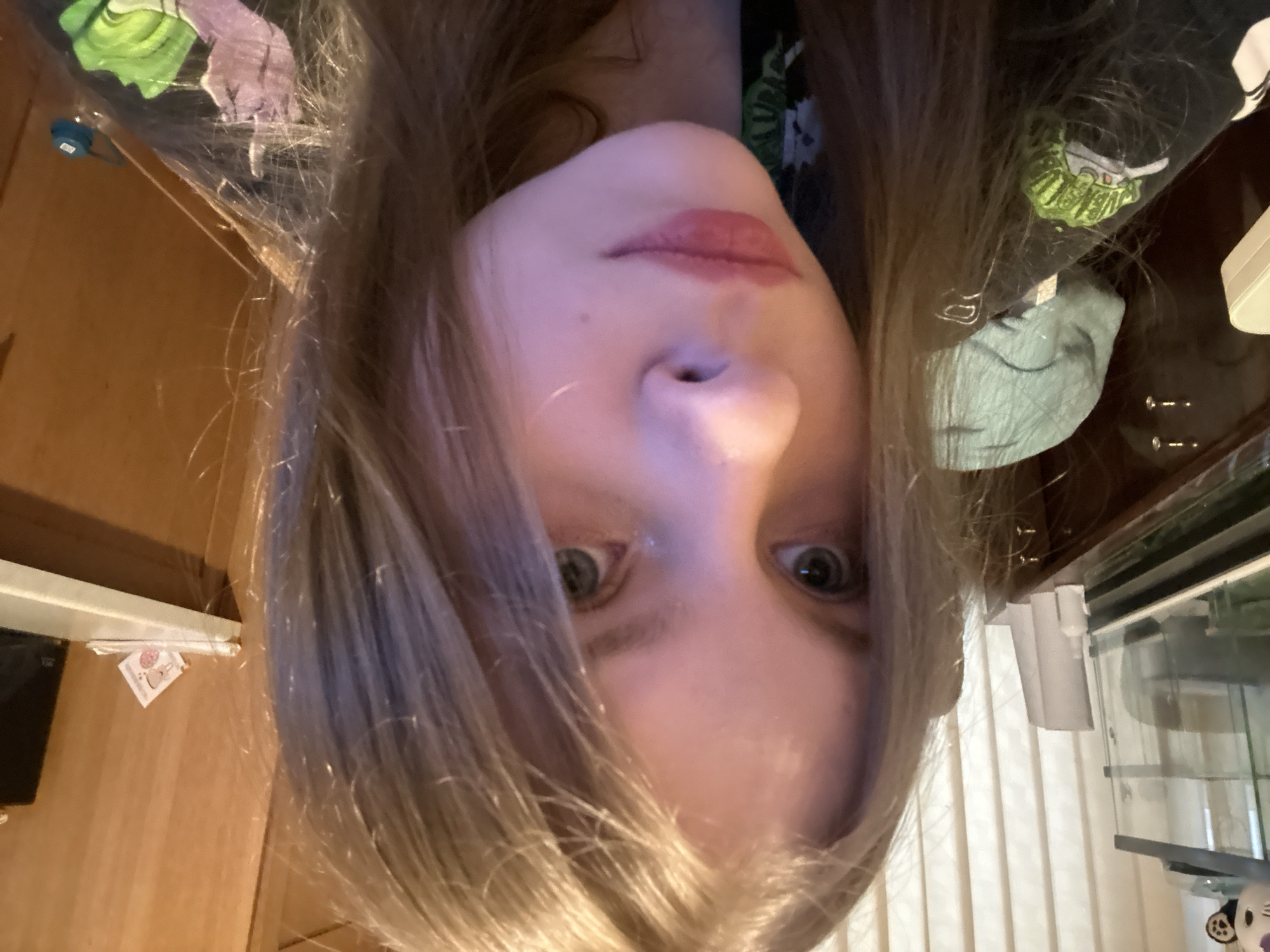 A photo of a person with blonde hair facing the camera. The person is positioned upside down. The person's face is visible from the nose up. Behind the person are various objects. Based on the available information, the location in Moscow, Russia, cannot be determined.