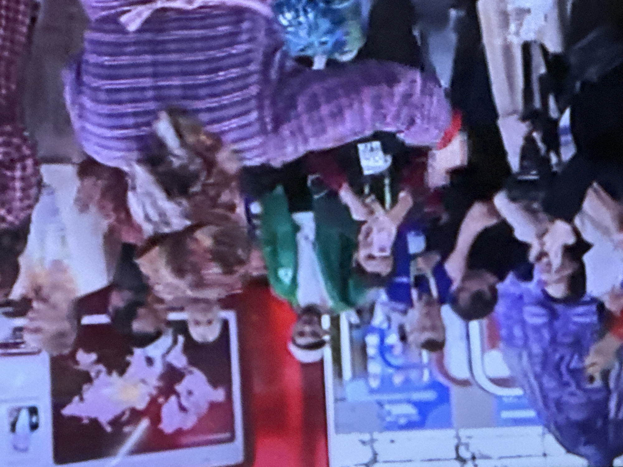 In Podolsk, Russia, a group of people are gathered indoors, possibly at an event or exhibition. The background features a large map of the world displayed on a screen. In the foreground, a person wearing a purple, horizontally striped garment with wide sleeves is facing away from the camera, with their arms outstretched. Other individuals are visible, some holding up phones, suggesting they are taking photos or videos. The overall atmosphere appears lively and dynamic, with a sense of shared experience among the attendees.