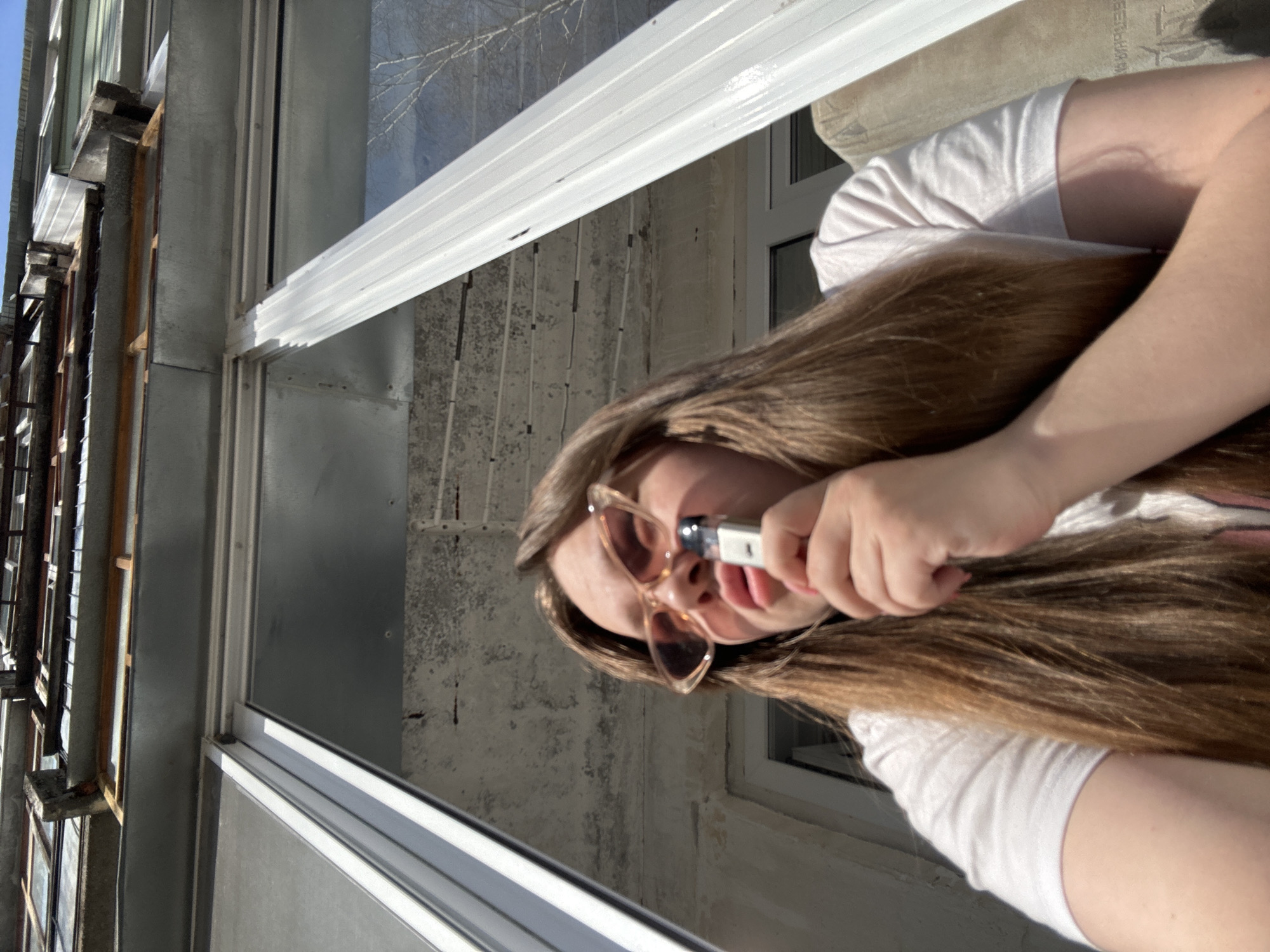 A young woman is visible, holding a lighter near her face. She is wearing sunglasses and has long brown hair. The location appears to be a building with a window. The specific location in the city of Chaikovsky, Russia, cannot be determined from the image.