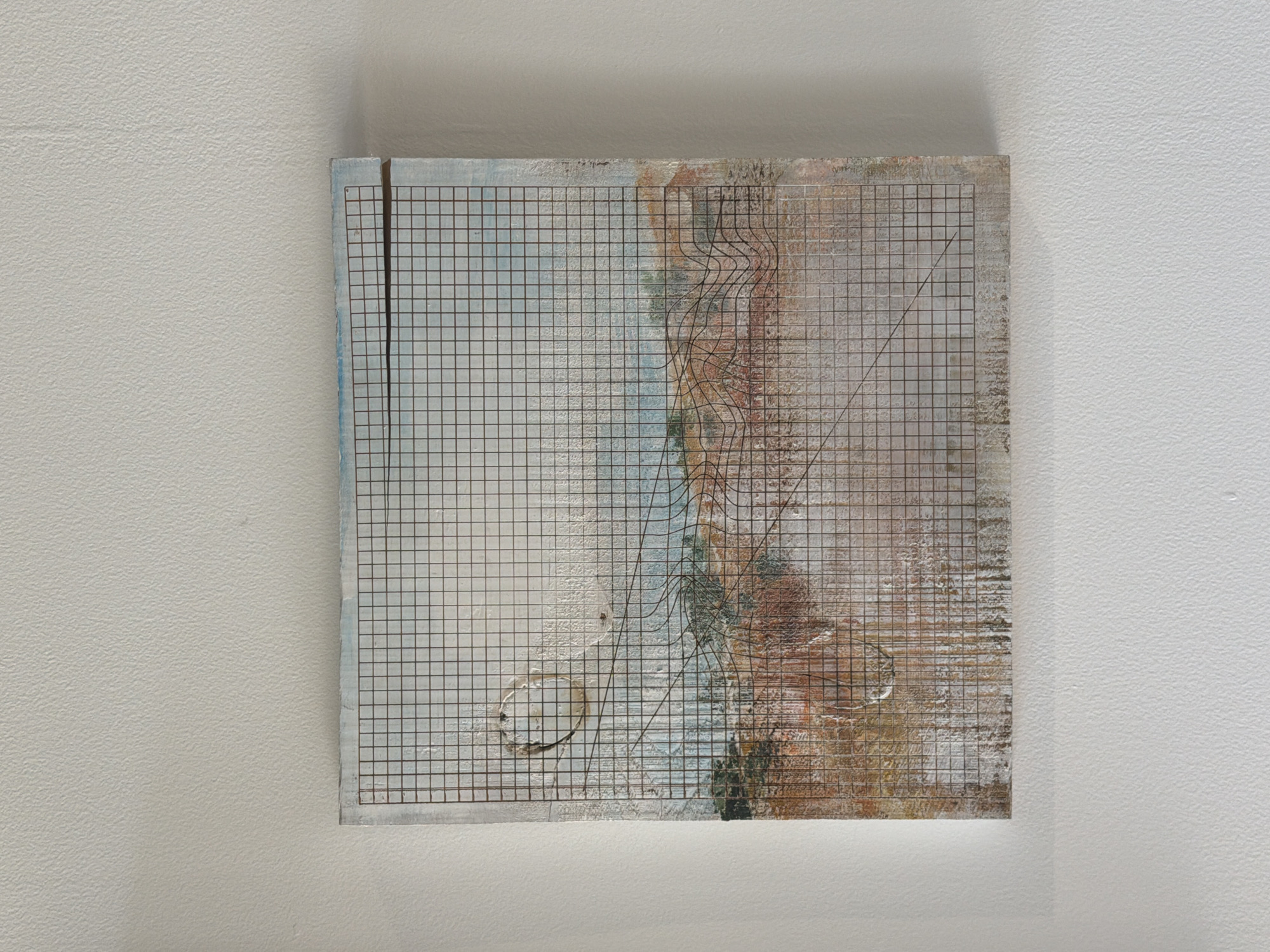 A square mixed-media artwork hangs on a white wall. The artwork features a grid pattern dominating the surface, with the left side primarily blue and white, transitioning to brown and beige tones on the right. There are distortions in the grid pattern, particularly a series of wave-like lines and circles. A diagonal line extends from the top right to the bottom left. The location is unknown.