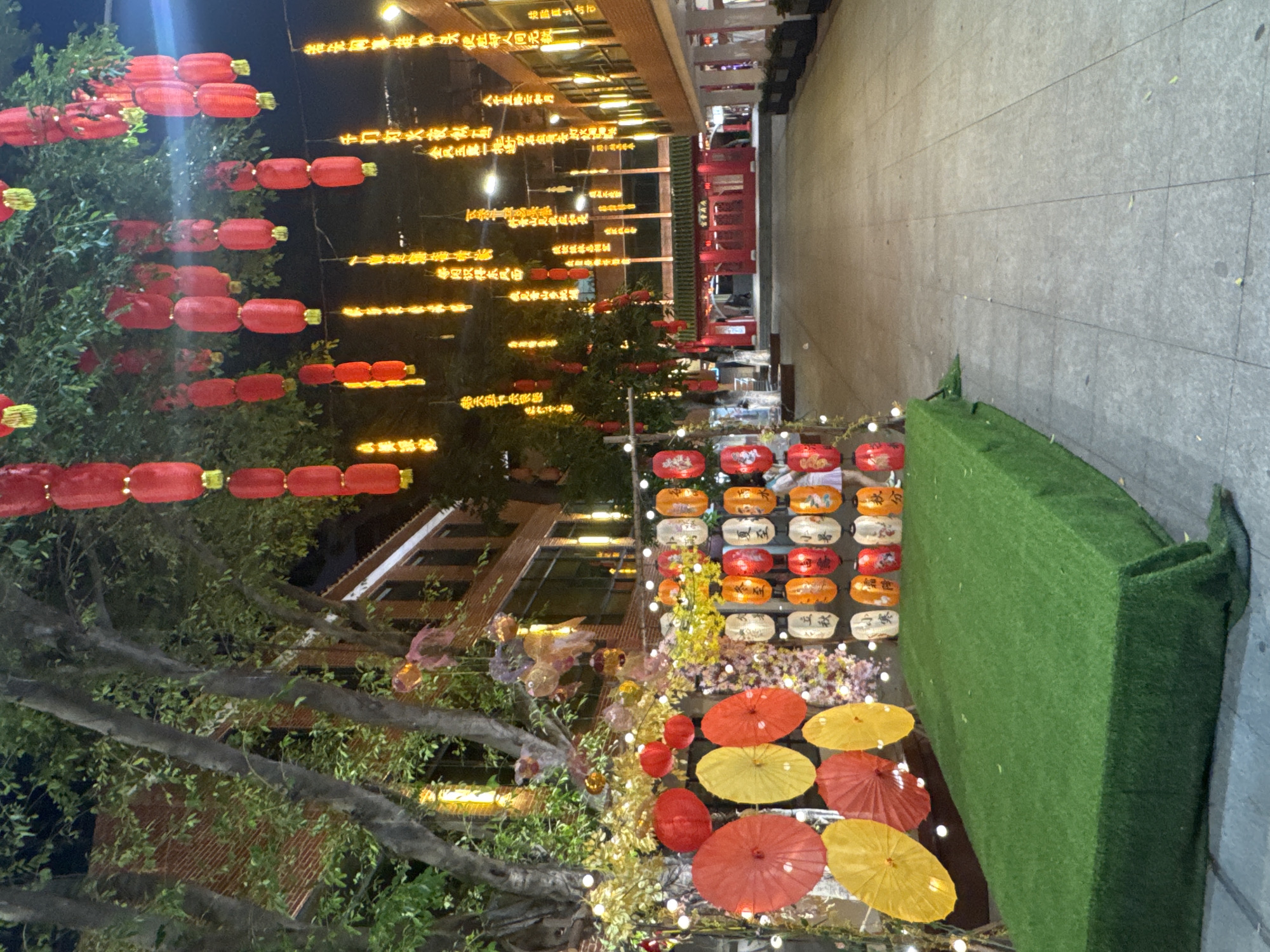 The image captures a vibrant scene likely in Yuexiu District, China, characterized by a festive atmosphere with decorations for a celebration or festival. Red lanterns hang in rows, both strung from trees and suspended above the street, contributing to a warm, illuminated ambiance. Lanterns with different colors such as orange, red, and white also add to the scenery. Additionally, yellow and red umbrellas are placed near the ground, enhancing the vibrancy of the decoration.
The image also features structures and buildings in the background, adding a sense of place to the setting. The buildings show the architecture of the district.
The scene is set at night, further emphasized by the use of bright decorations against the dark sky. Overall, the image portrays a lively and visually appealing representation of a cultural celebration or festival event.