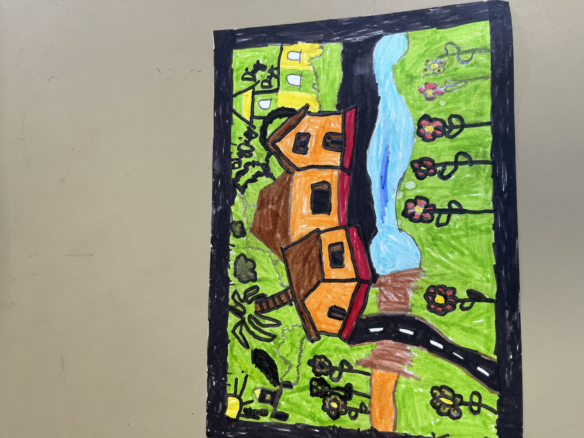 This is a colored drawing of a landscape. The scene depicts several houses with orange walls and brown roofs. A dark road with white stripes curves through the landscape. There is a body of blue water, possibly a river or lake, with green hills in the background. The foreground is filled with green grass and several red and yellow flowers. A palm tree is also visible. In the upper left corner, a yellow sun is drawn. The drawing is framed by a black border. The provided context of La Fouillouse, France, is not reflected in the visual elements of the drawing itself, as it is a generic landscape depiction.
