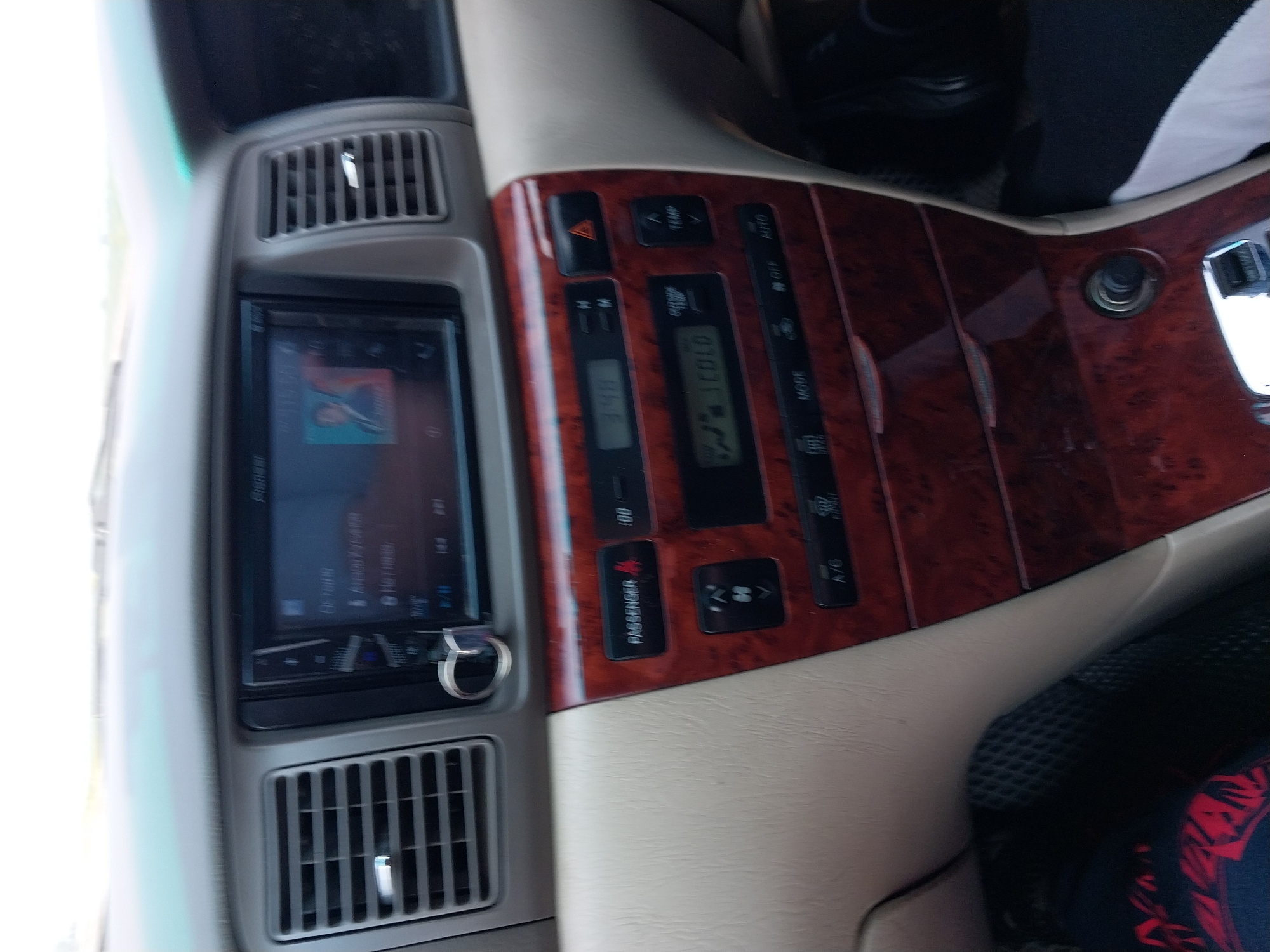 An interior view of a car's dashboard displays a central infotainment system, climate control, and other vehicle functions. The infotainment screen, a Pioneer model, shows music playback information and album art. Below it, a digital display shows "3:48" and climate control settings, including "OUTSIDE TEMP" and "COLD". Various buttons and knobs control functions like "PASSENGER", temperature adjustment ("TEMP"), hazard lights, and A/C. The dashboard is accented with a wood-grain trim. The image likely depicts the car's interior while parked or driving in Sychevka, Russia, though no specific indicators of the city are present.