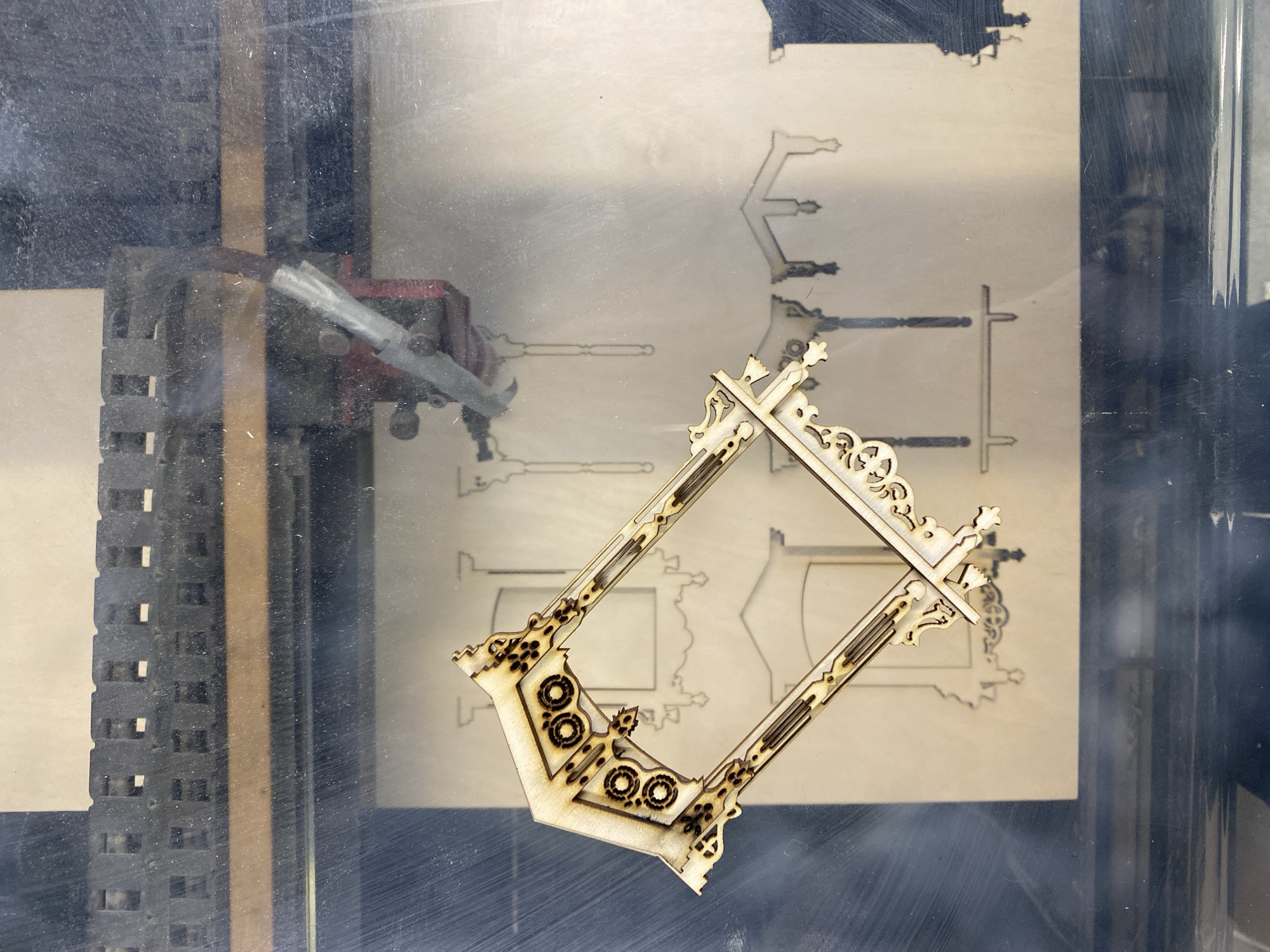 The image shows a laser cutter in operation. Inside the laser cutter's enclosure, a wooden frame has been cut out and sits on top of a larger piece of wood where its design was previously traced. The laser cutting head is visible to the left. The surrounding environment appears to be a workshop. There is no information visible indicating a location in Moscow, Russia.