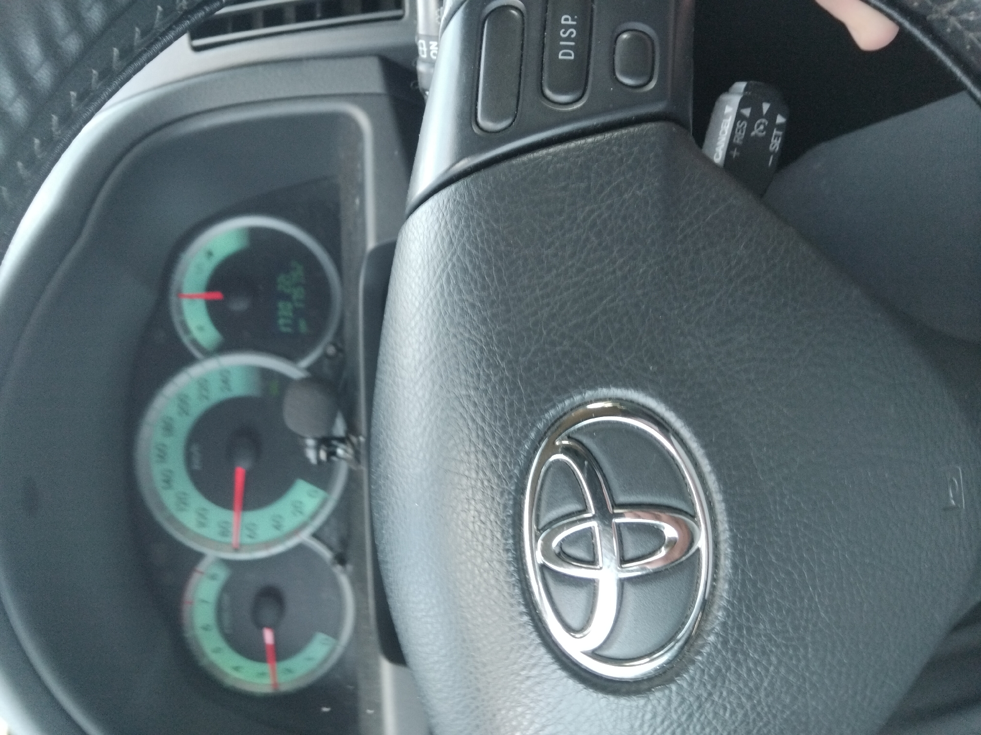 The image shows the interior of a Toyota vehicle, focusing on the dashboard and steering wheel. The speedometer reads approximately 60 mph, and other gauges are visible as well. The steering wheel features the Toyota logo and controls for cruise control and other vehicle functions. The car's odometer displays a mileage reading. The setting in Velchevo, Bulgaria cannot be determined from the available information.