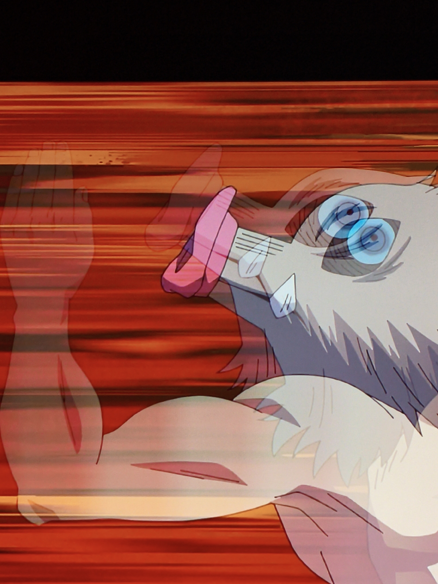 The image depicts an anime-style illustration of a character with a boar-like mask and large blue eyes. The character's mouth is open, and its tongue is extended. The background consists of horizontal red and orange lines, suggesting motion or speed. There are also faint, translucent outlines of what appear to be human limbs, possibly indicating the character is moving at a high velocity. The scene is a close-up shot, focusing on the character's face and upper body. The image does not contain any identifiable landmarks or elements that would indicate its location in Vladivostok, Russia.