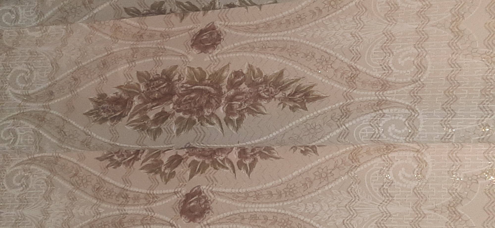 The image shows a close-up of a patterned fabric, likely a curtain or upholstery. The fabric has a floral motif with prominent roses and leaves in shades of brown and green, set against a lighter, possibly beige or cream-colored background. The pattern is intricate, with decorative elements and a damask-like quality. There are no people or any identifiable objects from Yessentukskaya, Russia visible in the image. The lighting is even, and the focus is sharp on the fabric's texture and pattern.