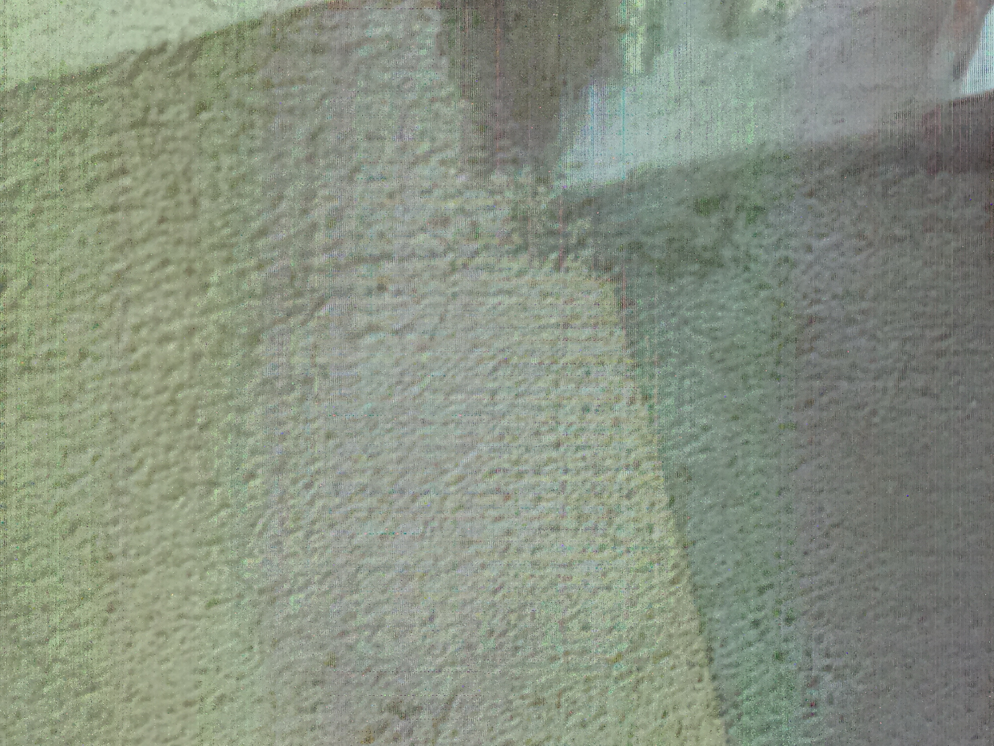 The image is a close-up, abstract shot of a textured surface, possibly a wall or fabric, with subtle variations in color and pattern. The overall tone is muted green and gray, with hints of yellow. There are visible lines or grain across the image, suggesting a digital artifact or the texture of the material itself. The image lacks any discernible objects, people, or specific environmental features that would allow for localization within Jalingo, Nigeria, or any other urban setting. The abstract nature of the image makes it impossible to identify any concrete details.