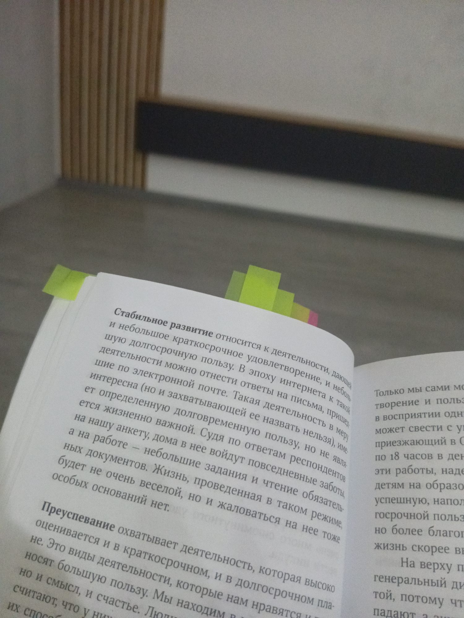 The image shows an open book with Russian text on its pages. Several lime green page markers are attached to the top edges of the pages. The book is resting on an out-of-focus surface. The first few lines of text on the left page reads: "Стабильное развитие относится к деятельности, дающей и небольшое краткосрочное удовлетворение, и небольшую долгосрочную пользу." The first few lines of text on the right page reads: "Только мы сами можем творение и польз в восприятии одн." The location in the city of Фоки, Russia is not identifiable from the image.