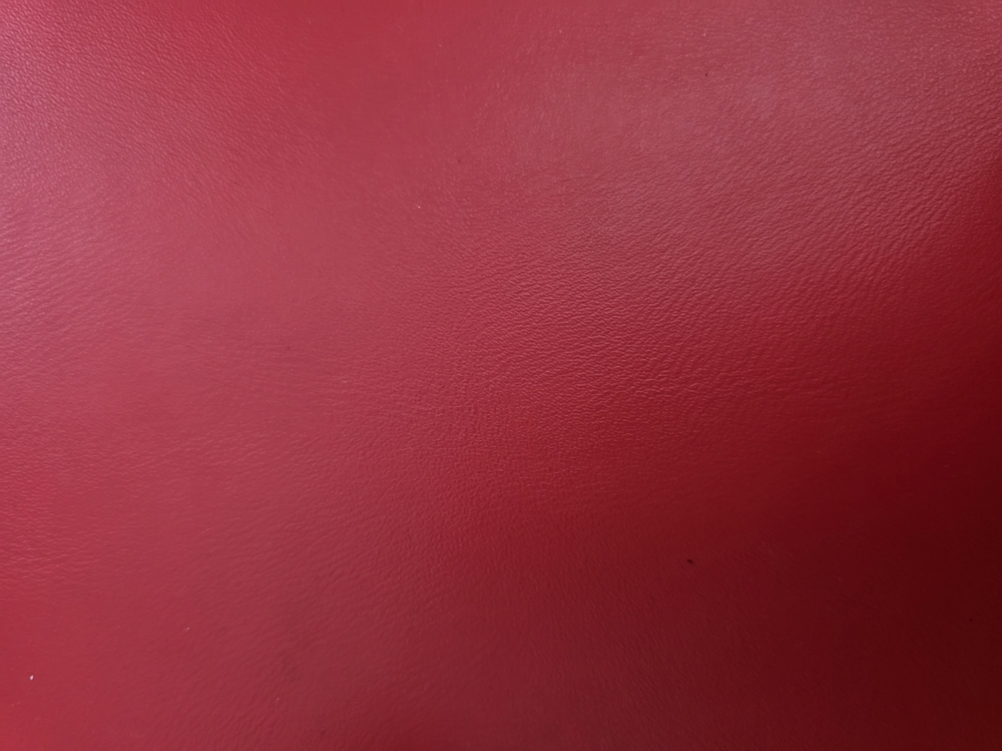 The image is a close-up, abstract shot of a red, textured surface. The texture appears to be that of leather or a similar material, with subtle creases and imperfections visible. The lighting creates a gradient effect, with the left side of the image being darker and fading into a brighter, more illuminated right side. There are no people, objects, or discernible environmental features that would indicate a specific location within the city of Kyiv, Ukraine, or any city for that matter. The image is purely a study of color and texture.