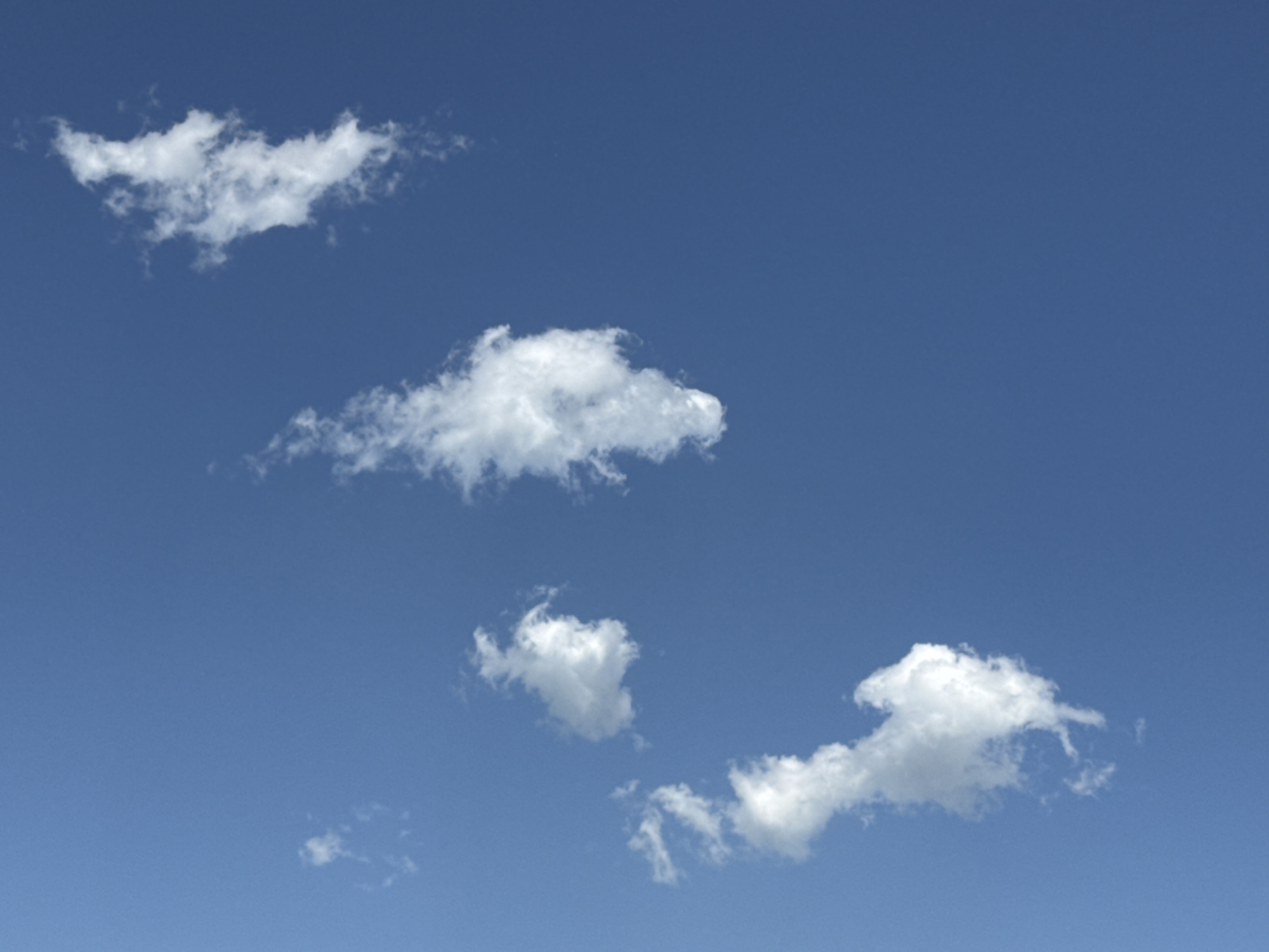 The image shows a clear blue sky with several scattered white cumulus clouds. There are no buildings, people, or any other objects visible in the frame. The clouds are spread across the upper and middle sections of the image. The cloud formation in the top left appears larger and more spread out than the others. The lower right portion of the image has two smaller cloud formations. The sky appears to be a typical daytime sky, possibly taken on a clear day in Calgary, Canada.