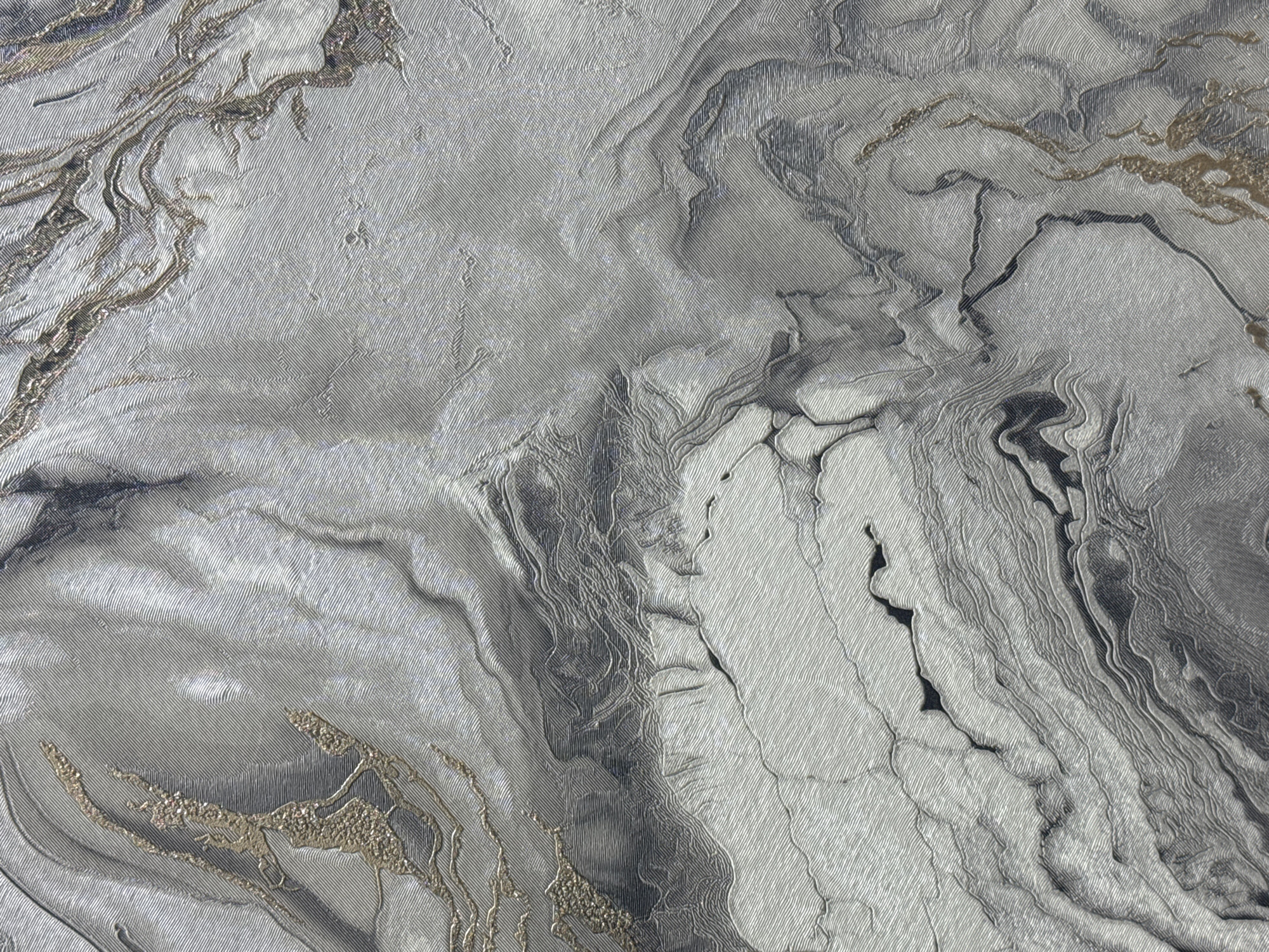 The image is a close-up of a textured surface resembling marble. The dominant colors are shades of gray and silver, with streaks of black and hints of gold. The surface appears to have a woven or fibrous texture overlaid with swirling patterns reminiscent of natural stone formations. No people, actions, or interactions are discernible in the image. There is no indication of the city of Saint Petersburg, Russia.