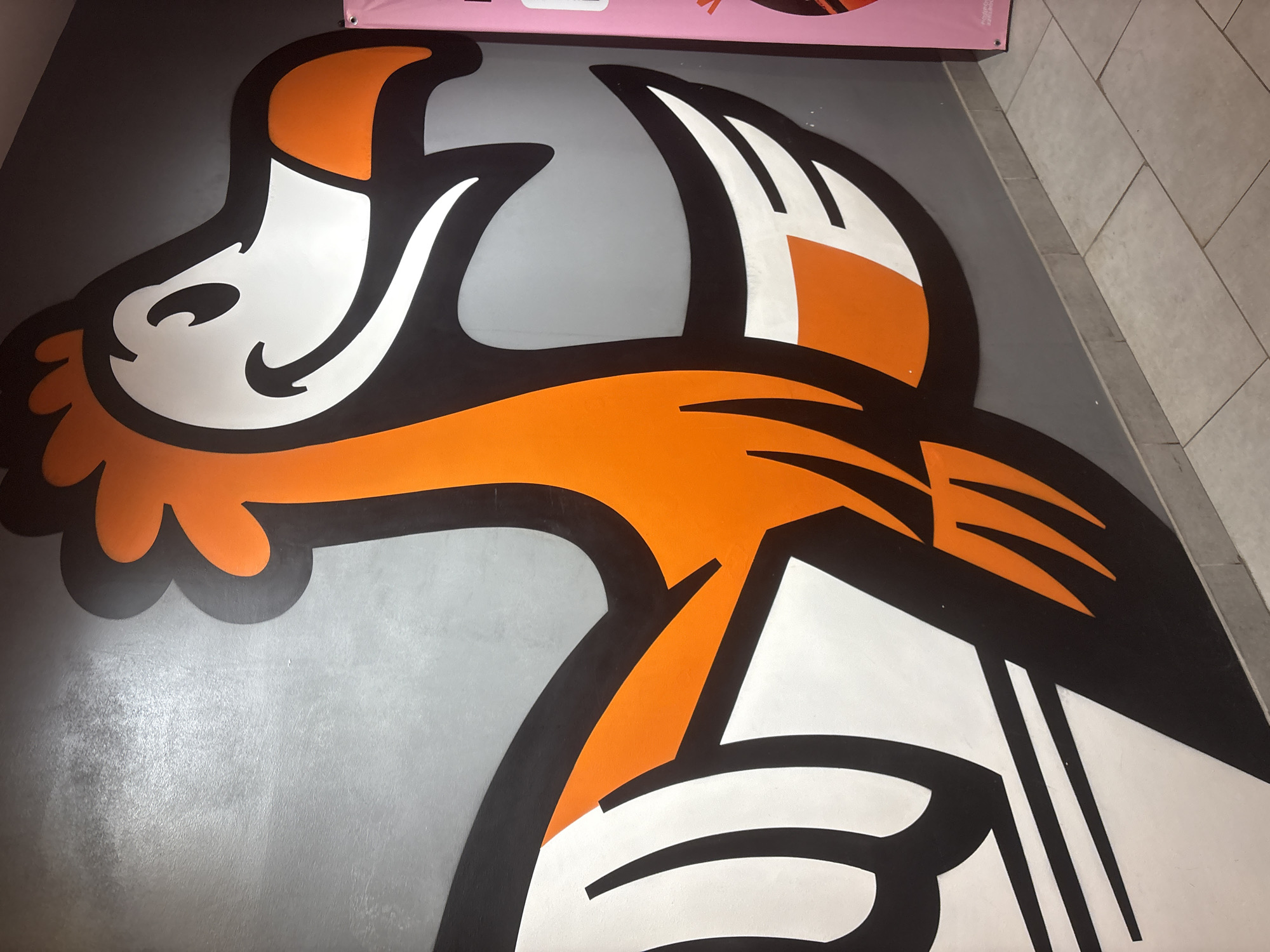 A large, stylized cartoon fox head graphic adorns a gray floor. The graphic features orange and white sections outlined in black. A small portion of a pink object is visible in the upper portion of the image. The floor is tile. The location is Votkinsk, Russia.
