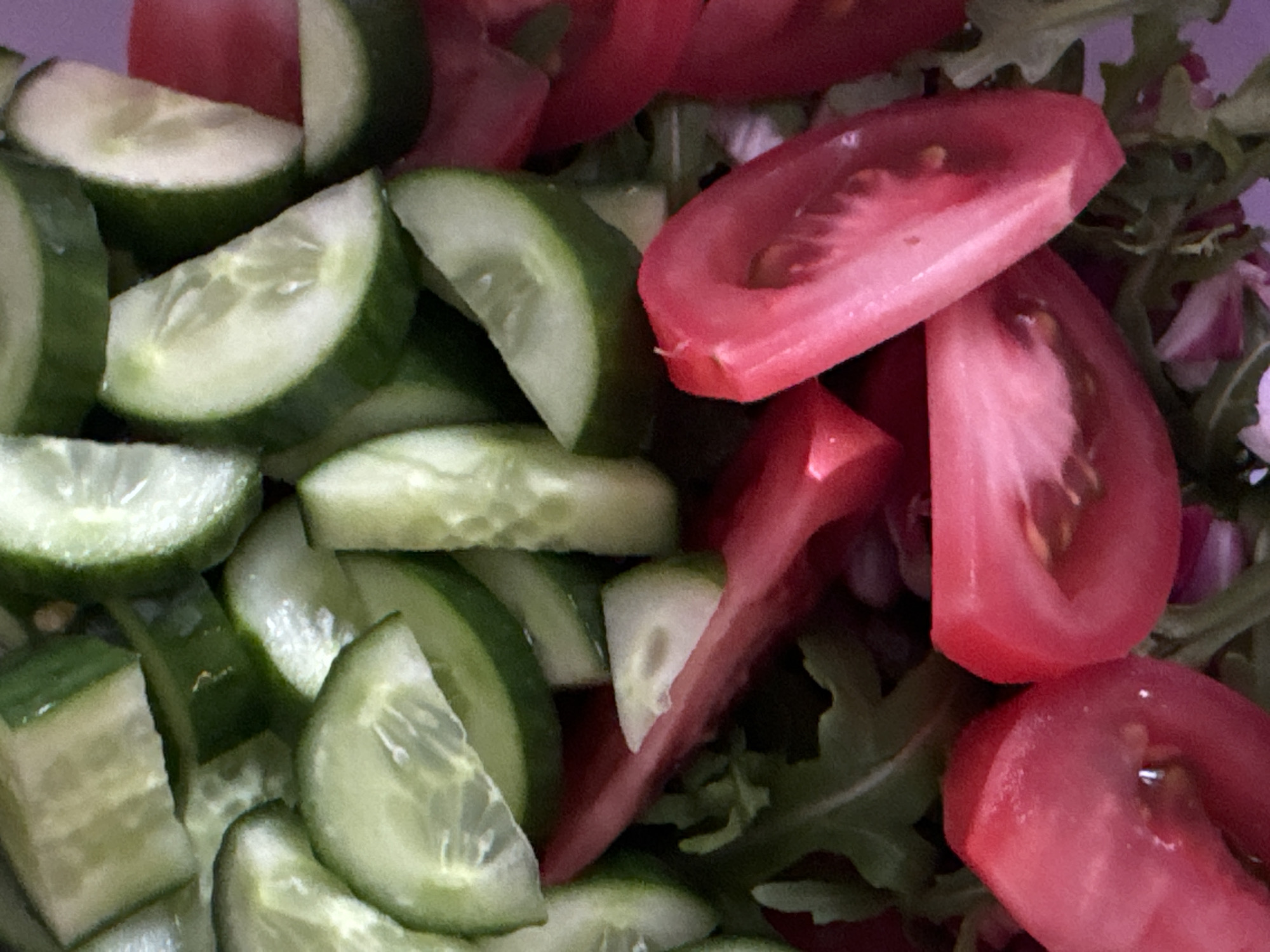 The image shows a close-up of a salad. The primary components of the salad are sliced cucumbers and tomato wedges. There is also some arugula in the salad. The scene appears to be indoors. There is no evidence to suggest that the image was taken in the city of Odintsovo, Russia.