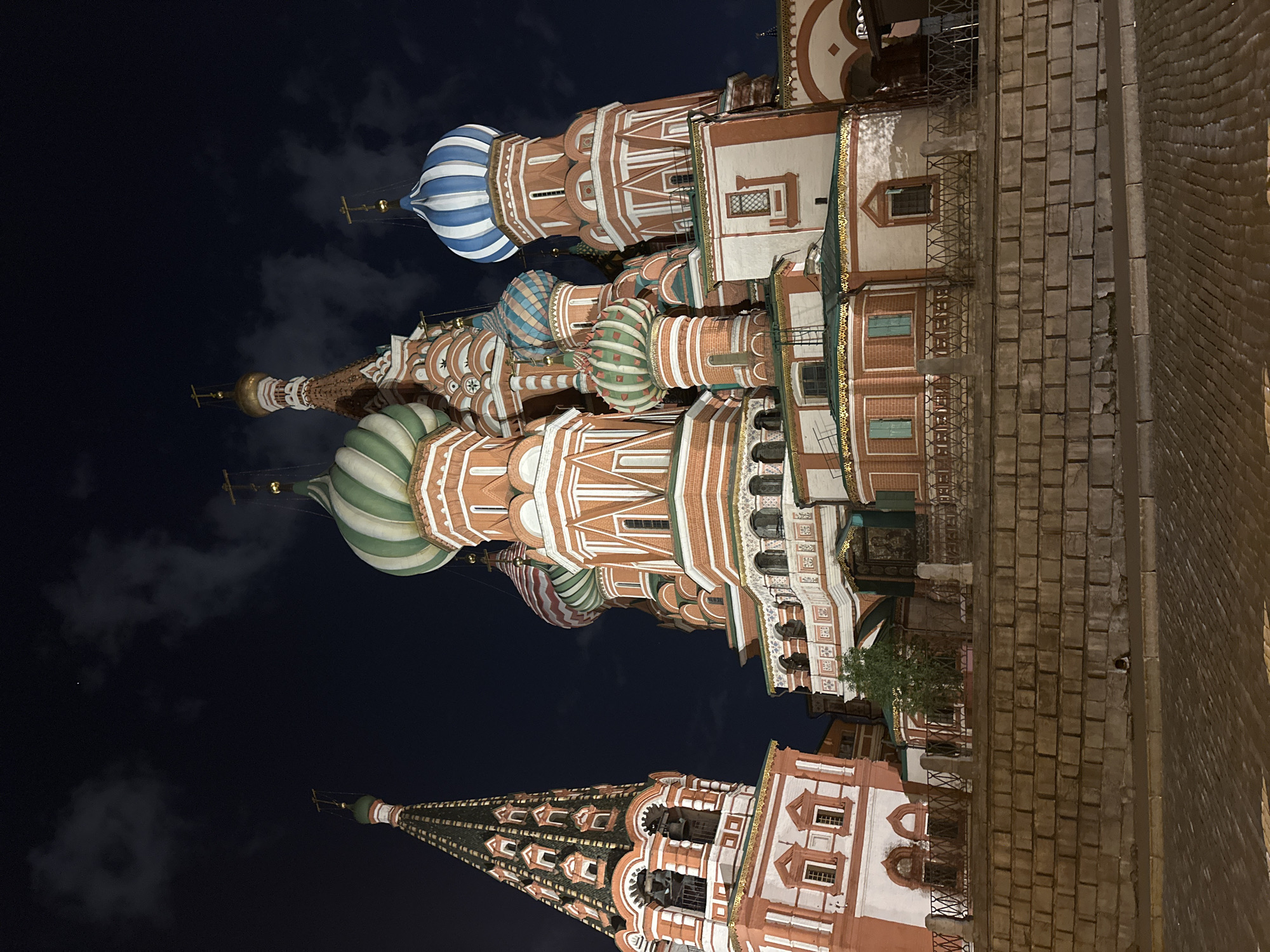 The image shows a view of St. Basil's Cathedral in Moscow, Russia, at night. The brightly colored domes and spires are visible against the dark sky. The building's architecture is intricate and ornate. The location is misidentified and should be Moscow, Russia, and not Woodmere, United States of America.