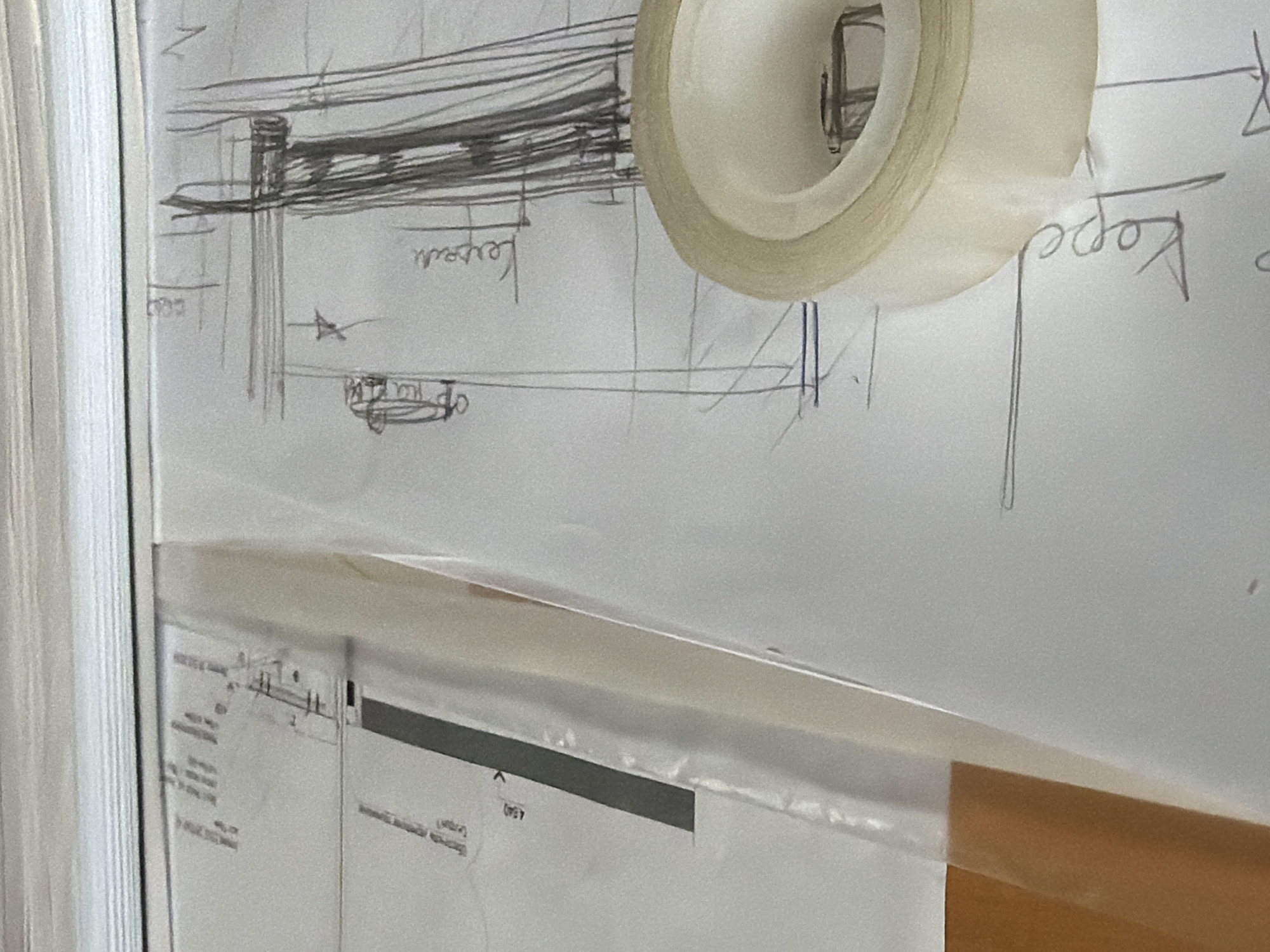 The image shows a close-up of a desk with architectural or technical drawings. A roll of clear tape is prominently featured in the foreground, partially covering a sketch. The sketches on the paper appear to be architectural plans or diagrams, with lines, annotations, and possibly representations of buildings or structures. One of the papers has text in Russian, and the context of Novo-daryino RAN, Russia, suggests the location of the office or workspace where these documents are being used. There are no people visible in the image. The environment appears to be an indoor office or studio setting.