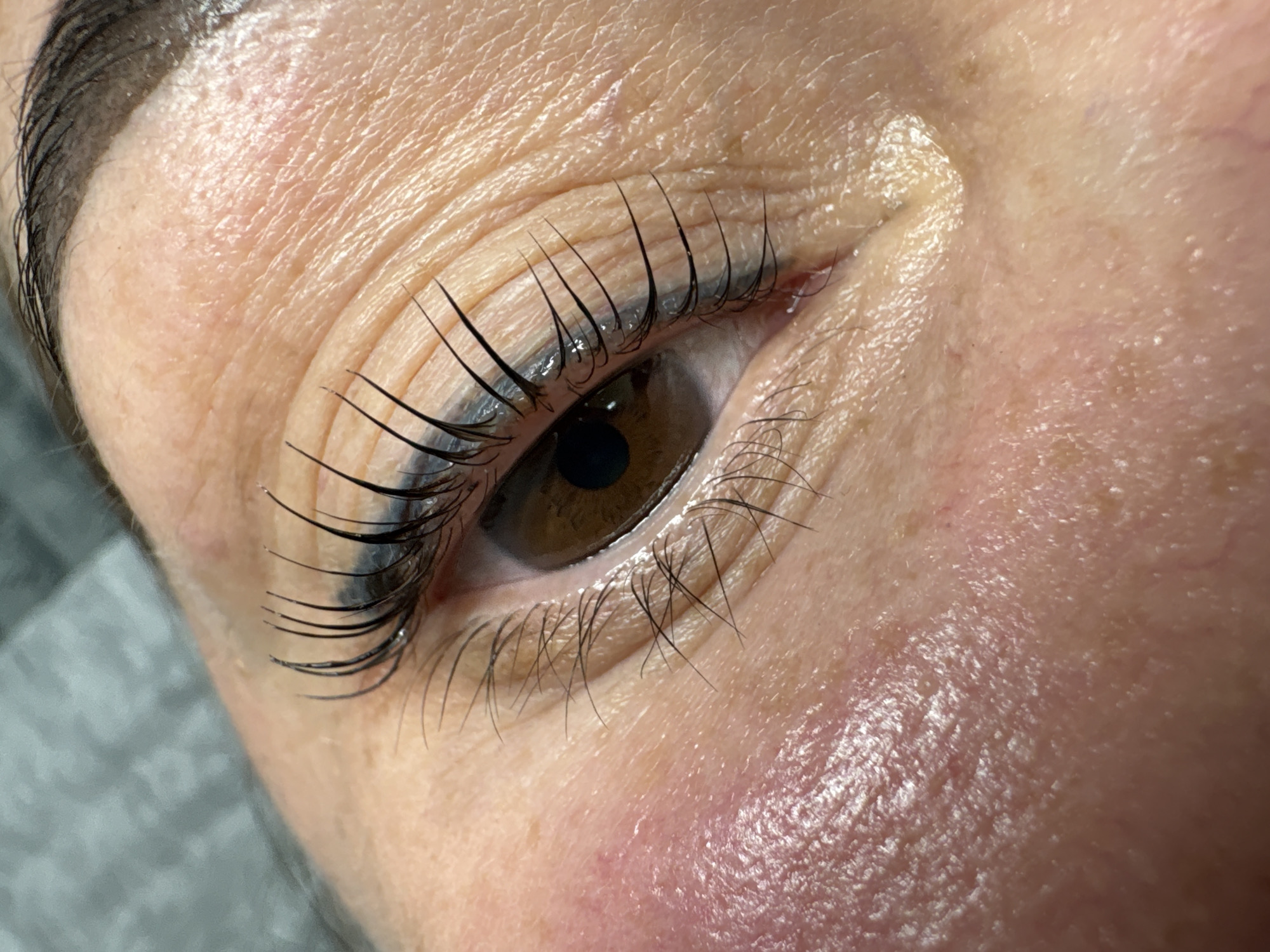 A close-up image captures a human eye, with focus on the long, dark eyelashes. The eye's iris is brown. The skin around the eye shows some wrinkling and fine lines. The lower portion of the skin displays some redness and a slightly rough texture. There is no context to indicate the location being the city of Perm, Russia.