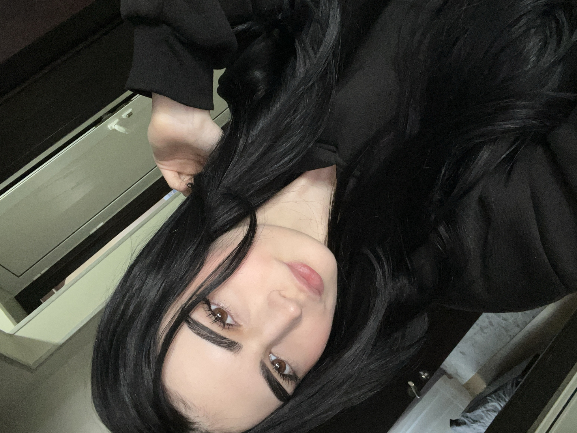 A selfie of a young woman with fair skin, brown eyes, and black hair. She is wearing a black top. The background features a pale wall and what appears to be the edge of a cabinet or doorframe. There is no information available to determine the location within Burgas, Bulgaria.