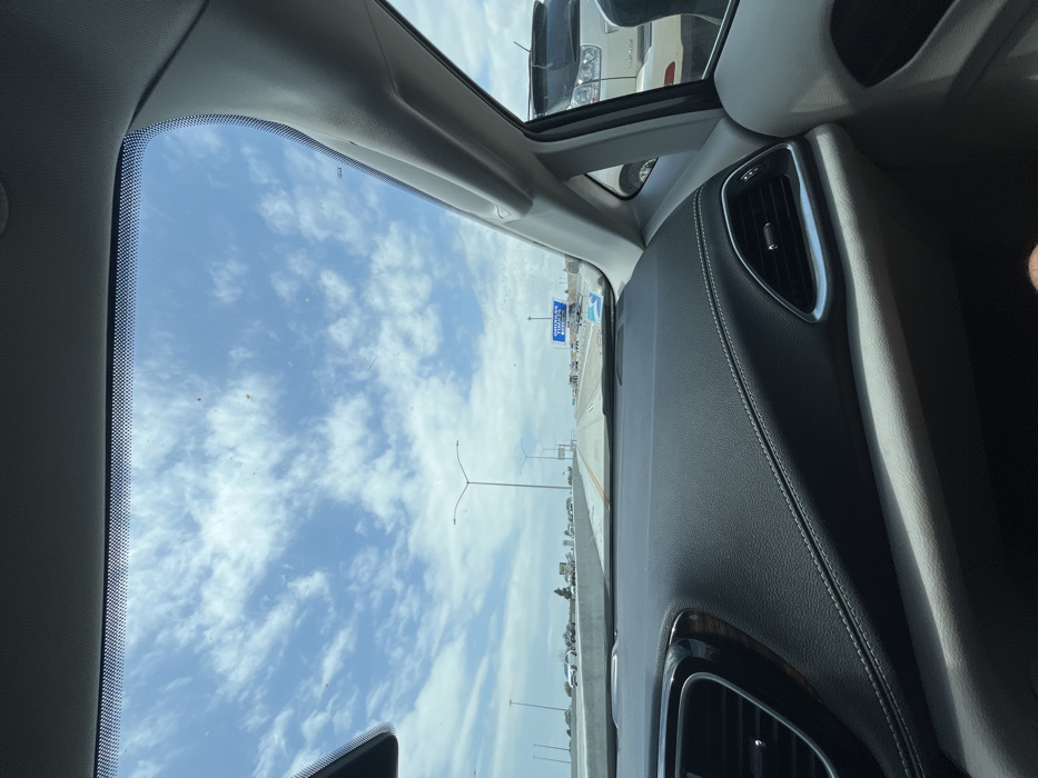 The image shows a view from the driver's seat of a car, looking out the windshield at a highway. The sky is blue with white clouds. The highway is clear, with light traffic. There are a few street lights visible. A sign for "American Airlines Arena" is visible on the right side of the highway. The car is parked near a large building, and there are trees and bushes in the distance. The image was taken in Westminster, California, at the coordinates 33.743, -118.003. A person's leg can be seen in the bottom right corner of the image. The car's interior is black leather. The image was taken during the day, under sunny conditions. The person is wearing a white shirt and blue jeans. The car is a modern vehicle with a sunroof. The highway is a four-lane road with a concrete barrier. The image is taken from a vehicle in motion, as the highway appears to be moving. The image is taken from a low angle, as the horizon is visible in the distance. The overall composition of the image is dynamic, with a sense of movement and motion. The subject of the image is the view from the driver's seat of a car, and the composition of the image reflects this. The image is well-composed and provides a clear and concise view of the scene. It is well-lit and the colors are vibrant. The image is sharp and clear.