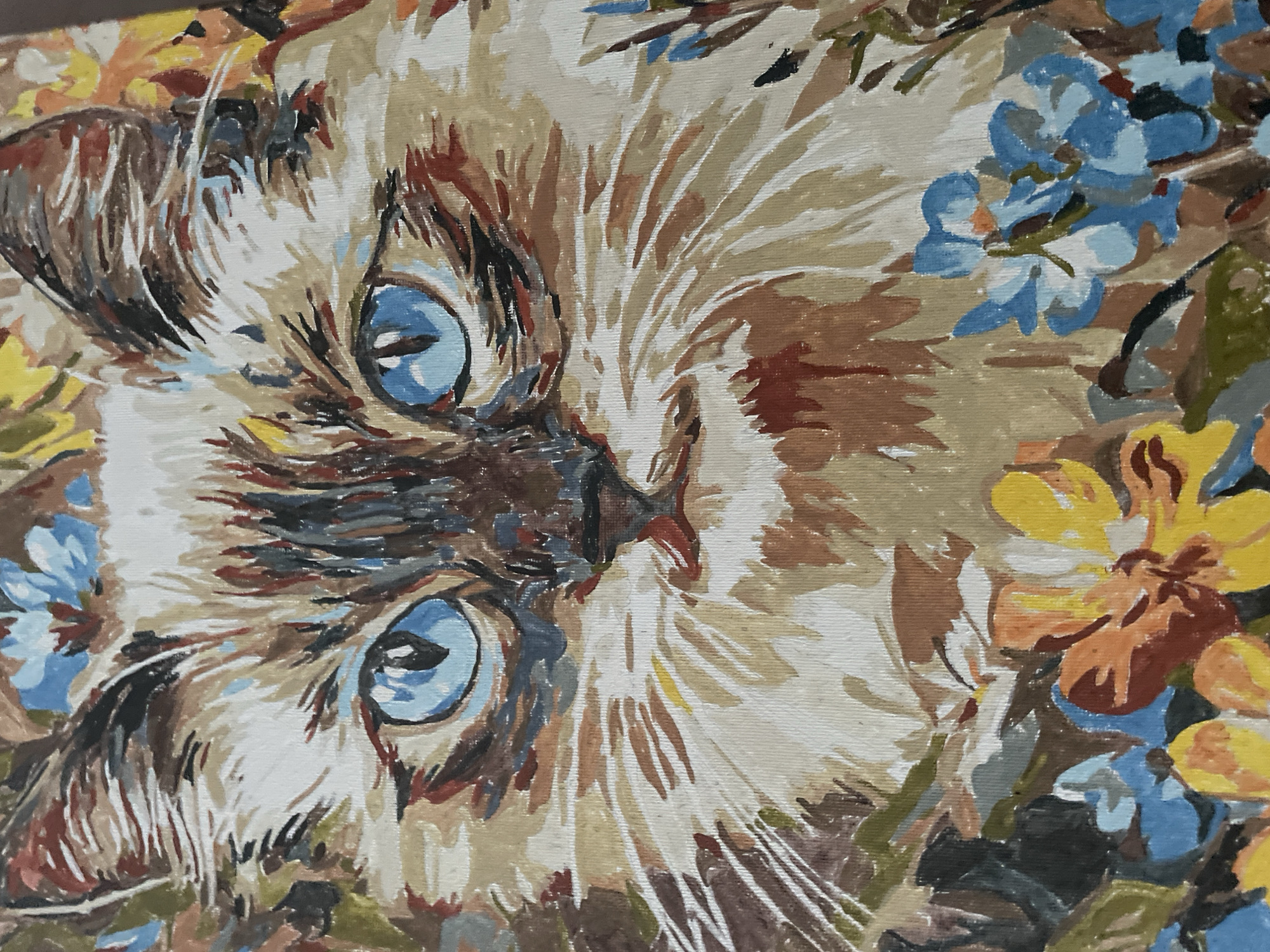 This is a close-up, two-dimensional painting of a cat's face, rendered in a textured, impressionistic style with visible brushstrokes. The cat has striking blue eyes, a brown and white patterned coat, and whiskers. The background is filled with colorful flowers and foliage in shades of blue, yellow, orange, and brown. The painting appears to be on canvas and exhibits vibrant colors. The origin or location of this painting within the city of Rivne, Ukraine, is not discernible from the image itself.